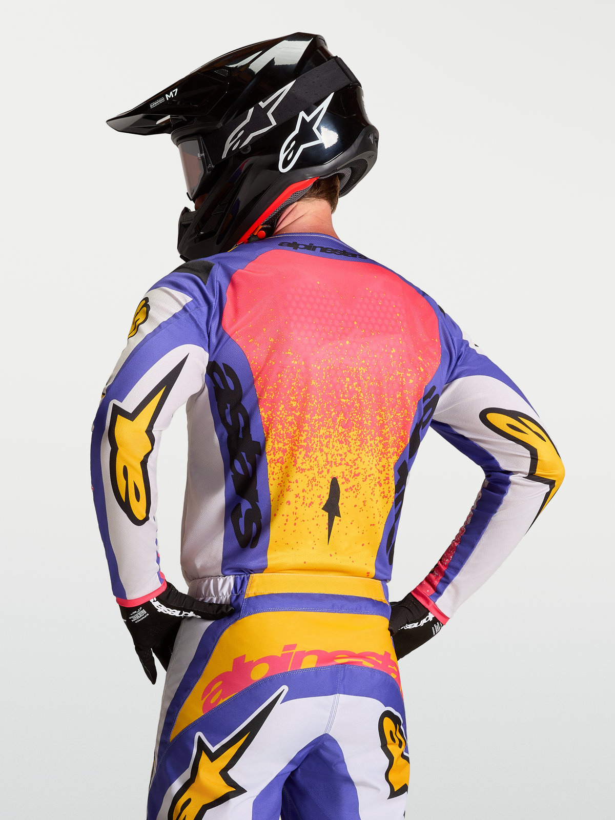 Alpinestars Fluid Drag Trikot in Blau und Gold, Rückansicht an einem Model mit Helm, Motocross-Jersey mit ergonomischem Rückenschnitt und feuchtigkeitsableitendem Material.