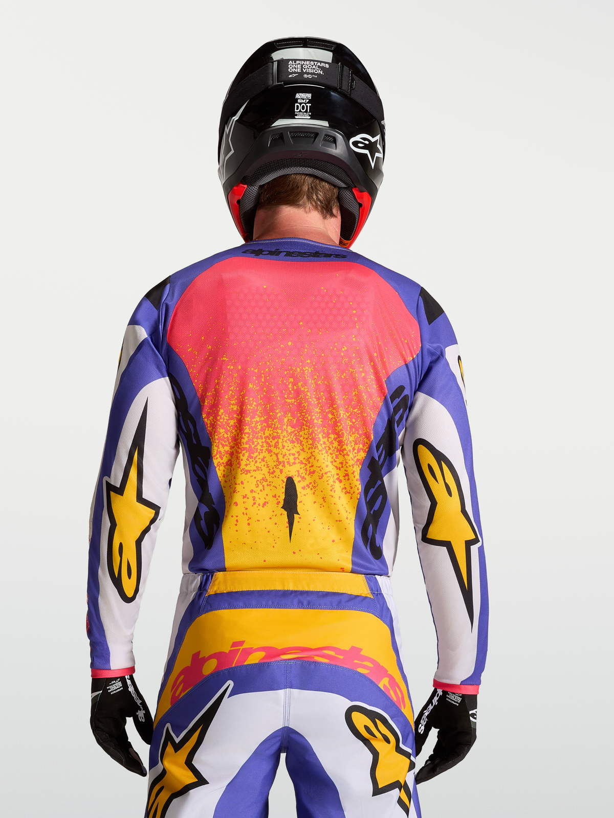 Alpinestars Fluid Drag Trikot, Motocross-Ausrüstung für Herren in Lila und Blau mit Gold, Rückansicht am Model mit passender Hose und Helm.