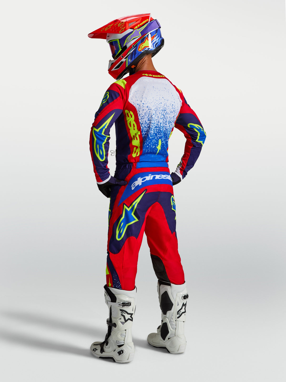 Alpinestars Fluid Drag Trikot, Herren-Motocross-Oberteil, Blau und Rot, Rückansicht mit passender Ausrüstung und weißen Stiefeln.