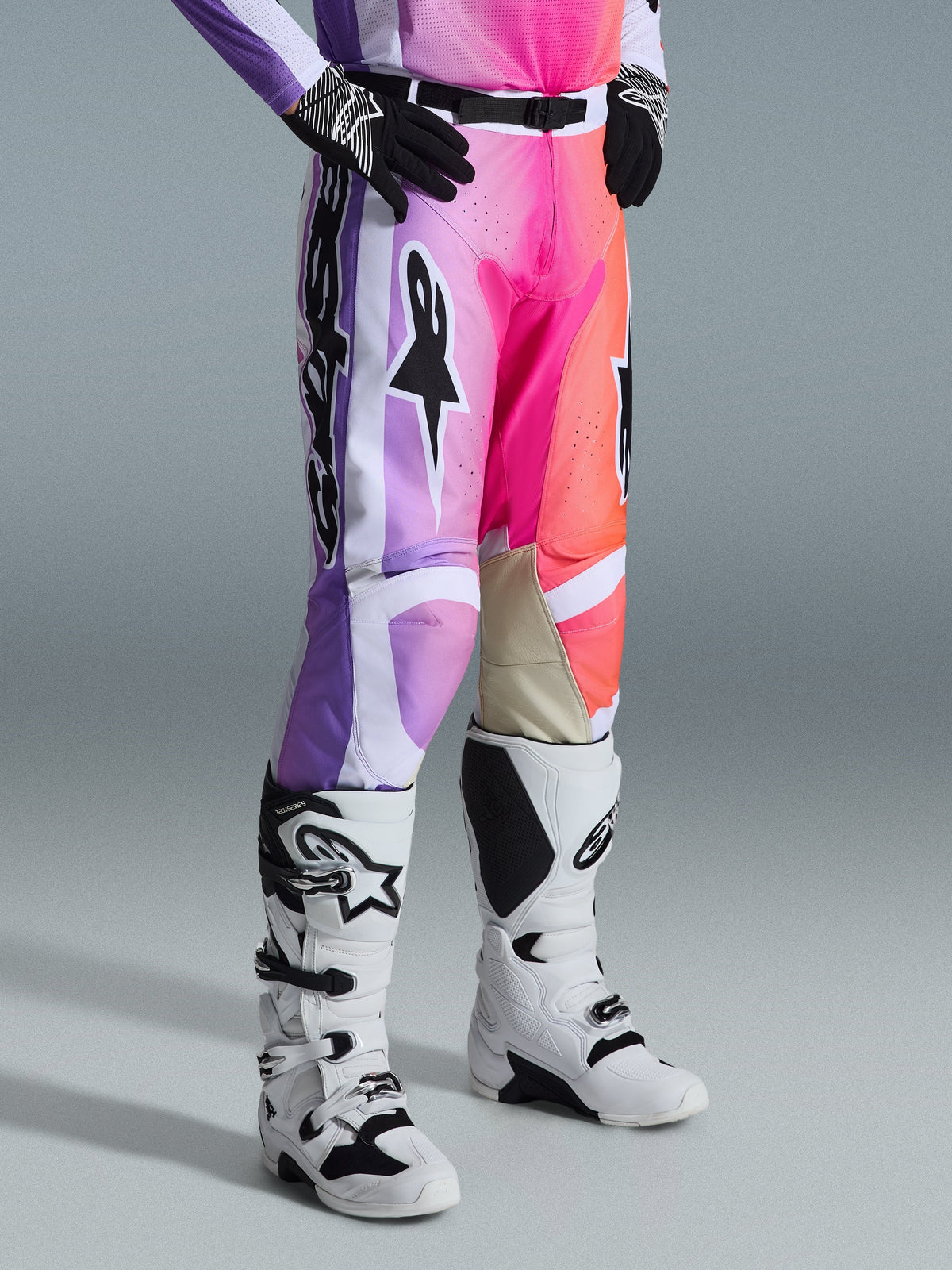 Alpinestars 2026 Racer Air Portl Hose, Motocross-Hose, mehrfarbige Grafik mit lila, pinken und orangefarbenen Farbverläufen, kombiniert mit weiß-schwarzen Motocross-Stiefeln und schwarzen Handschuhen, sportliches Race-Fit-Design und hellbraune Leder-Innenknieeinsätze.
