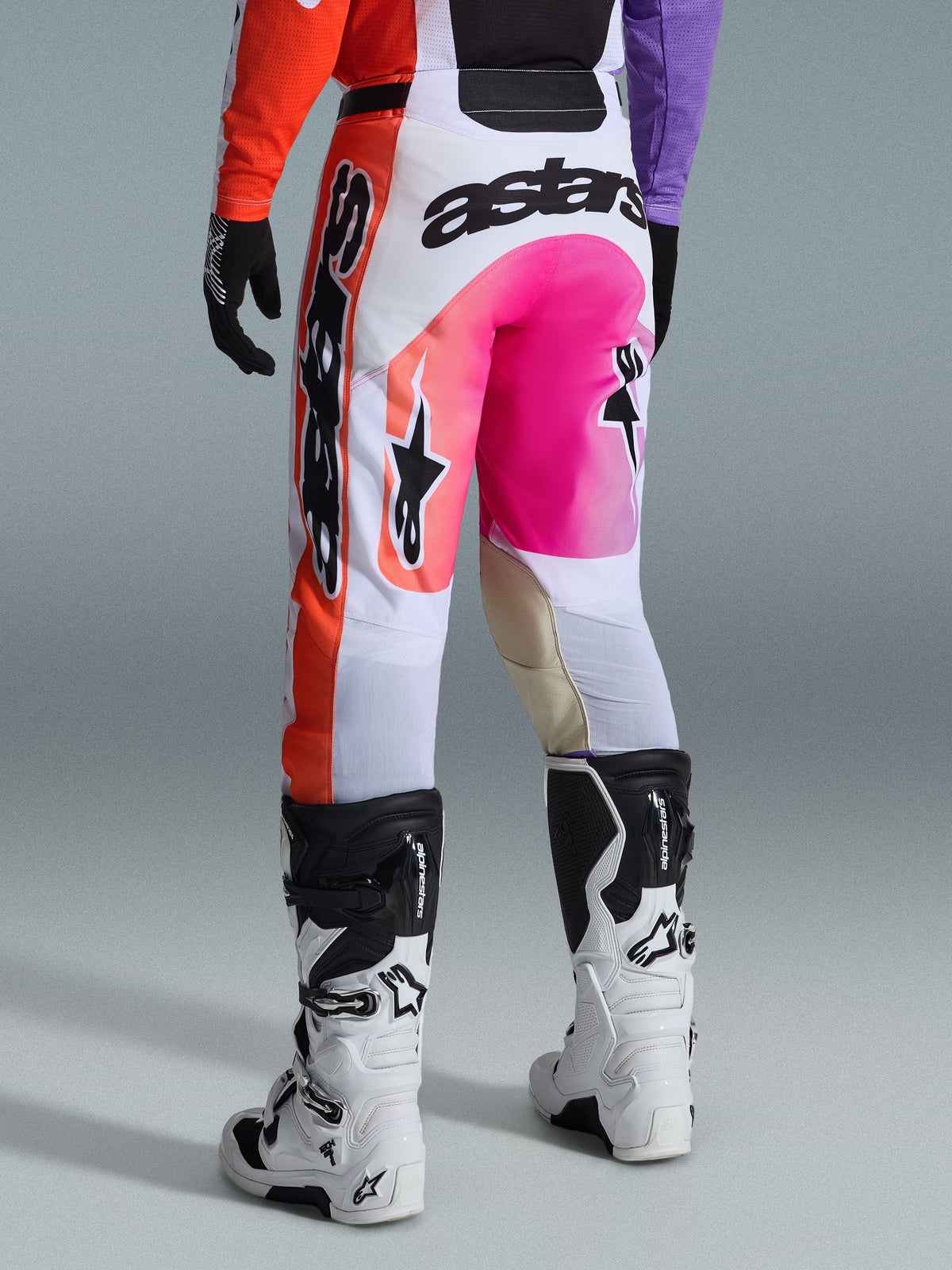 Alpinestars 2026 Racer Air Portl Hose, Motocross-Hose, Mehrfarbig mit Weiß, leuchtendem Pink und Orange, Rückansicht getragen mit weißen und schwarzen Alpinestars Stiefeln, auffälliges Branding und strapazierfähige Racing-Konstruktion
