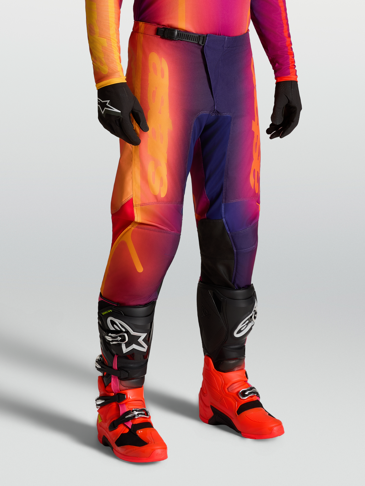 Alpinestars Fluid Kepler Hose, Offroad-Motocross-Hose in Lila und Orange, sportliche Passform, getragen mit Tech-Stiefeln und Handschuhen.
