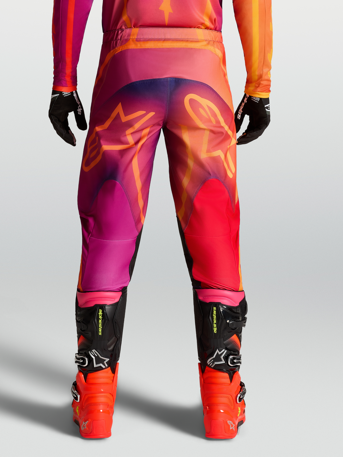 Alpinestars Fluid Kepler Hose, Motocross-Hose für Herren, Lila und Orange, mit Stern-Grafiken am Gesäß und schwarzen MX-Stiefeln.
