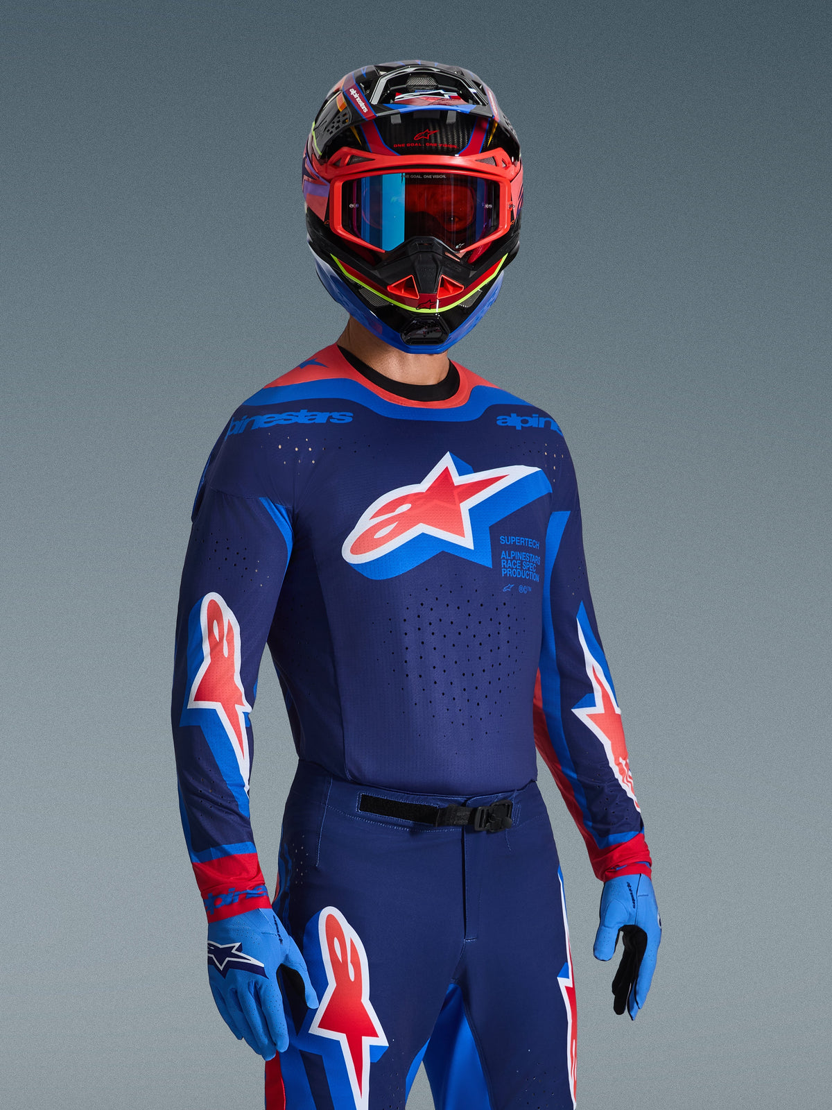 Alpinestars 2026 Supertech Vista Gear Set, Motocross rider wearing a dark blue jersey with light blue and red accents and a large star logo on the chest, matching pants and gloves, multi-colored helmet with blue and red goggles, pro-level racing apparel.