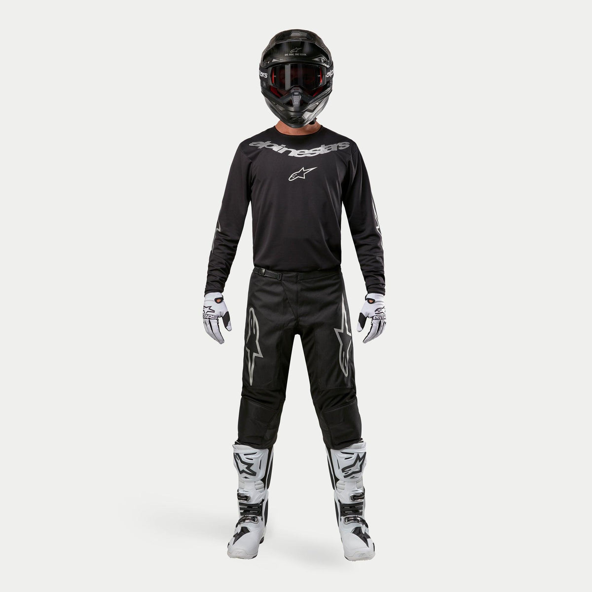 Motocross-Fahrer in kompletter Rennausrüstung, Alpinestars 2024 Fluid Graphite Trikot in Schwarz-Silber, schwarze Hose mit silbernen Stern-Logos, schwarzer Helm mit roter Brille, weiß-schwarze Stiefel, weiß-schwarze Handschuhe, abgestimmtes Motocross-Outfit