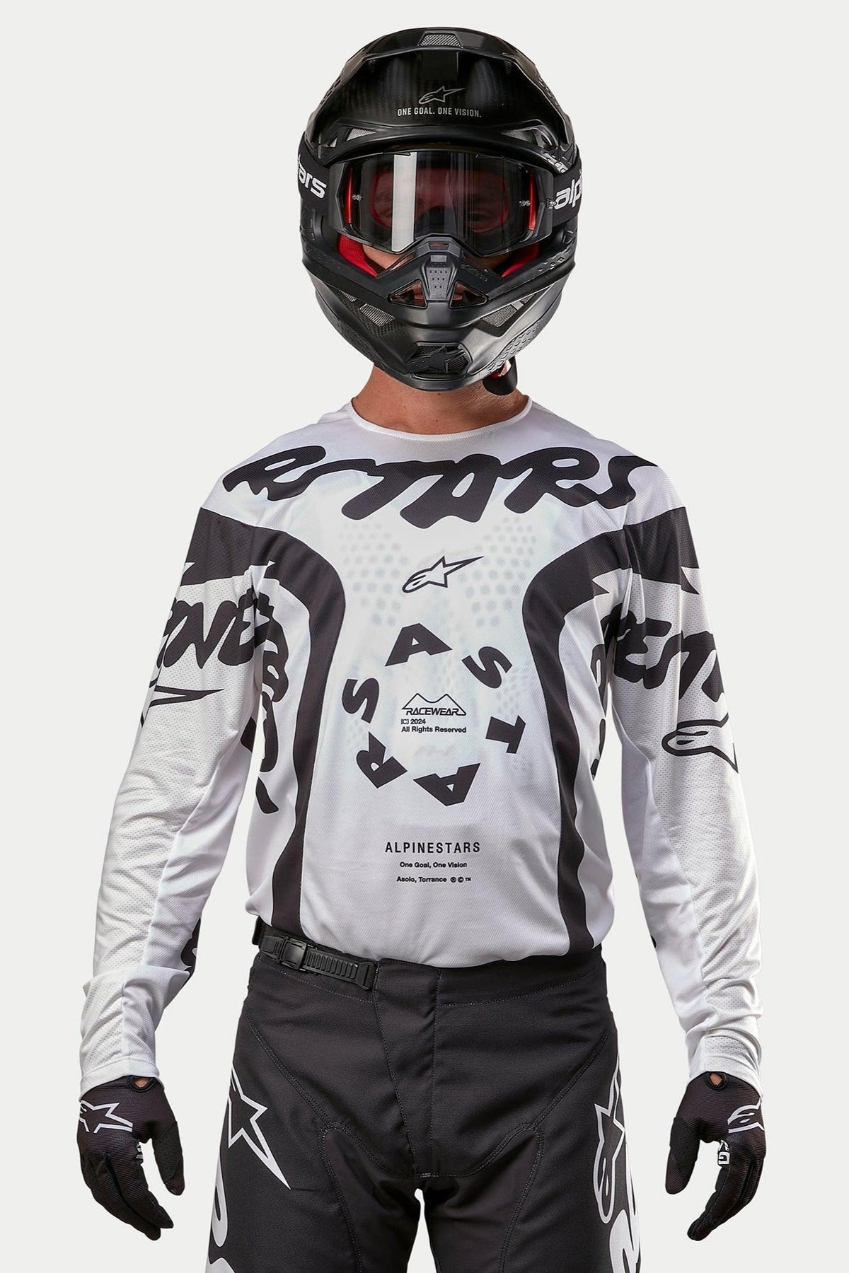 Motocross-Fahrer im Alpinestars 2024 Racer Hana Jersey in Weiß und Schwarz, kombiniert mit einem schwarzen Helm und einer schwarzen Motocross-Hose, mit markanten schwarzen „ASTARS“-Grafiken und einem kreisförmigen zentralen Logo, professionelle Offroad-Rennausrüstung