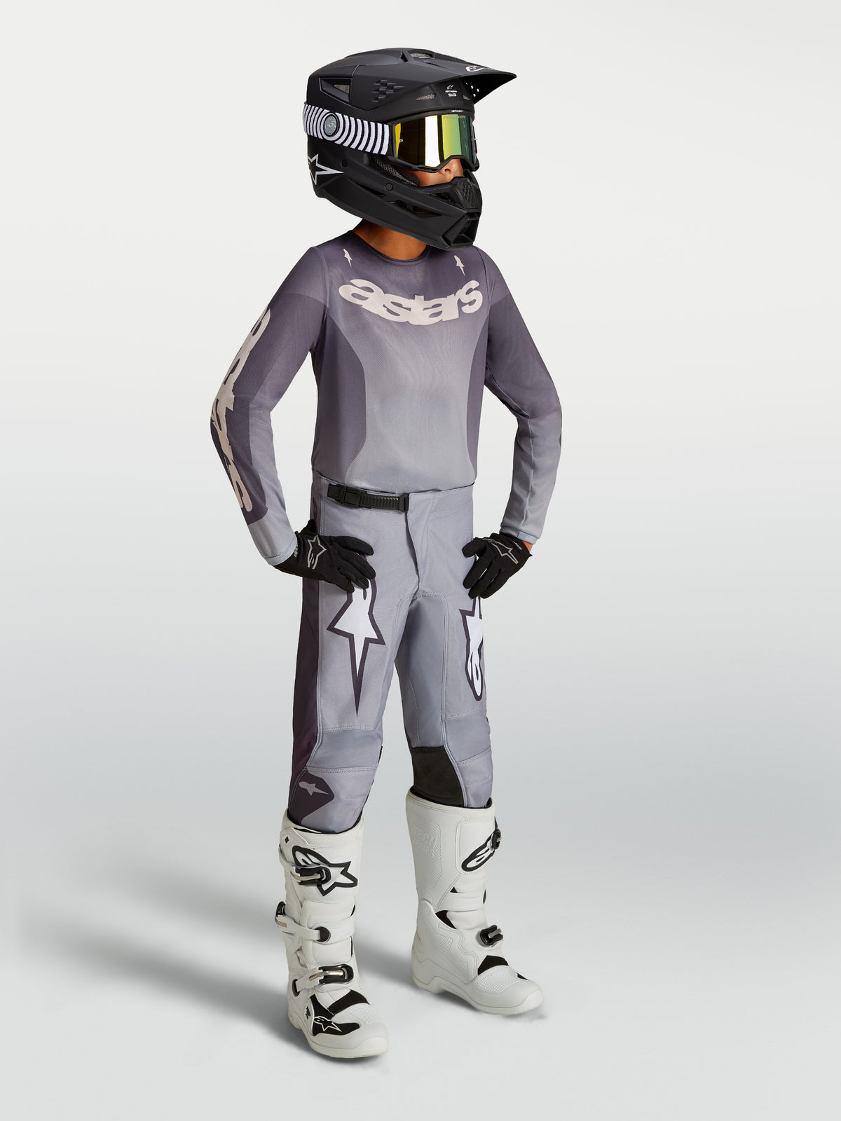 Alpinestars Youth Fluid Amber Gear Set, gray motocross jersey and pants with white racing boots and black helmet.