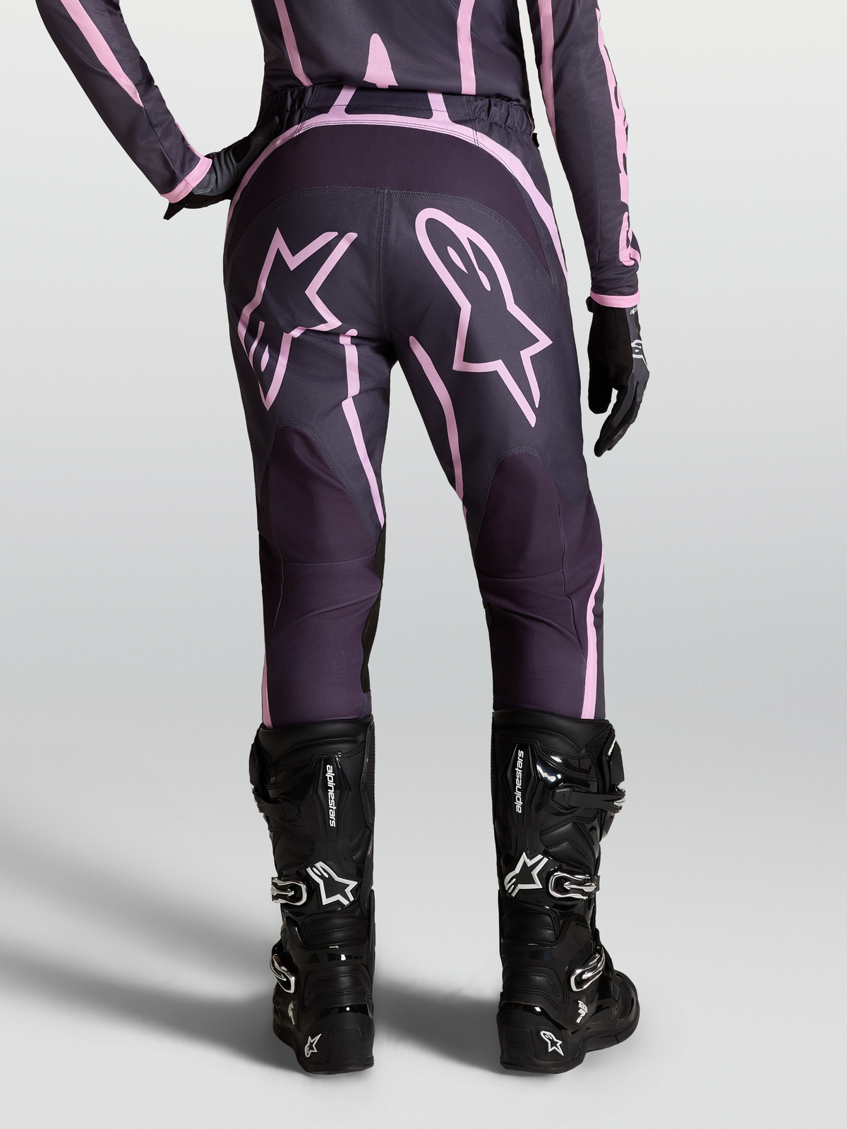 Alpinestars Stella Fluid Apex V2 Hose, Damen-Motocross-Hose in Grau und Pink, mit Sterngrafiken am Gesäß und schwarzen MX-Stiefeln, Rückansicht am Model.
