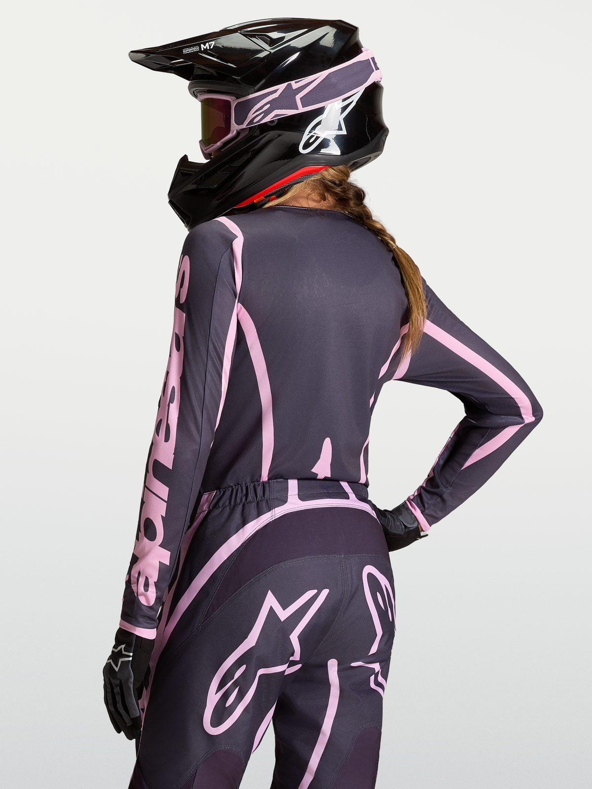 Alpinestars Stella Fluid Apex V2 Trikot für Damen, Motocross-Ausrüstung in Grau und Pink, feuchtigkeitsableitendes Material, On-Model mit passender Hose und schwarzem Helm.