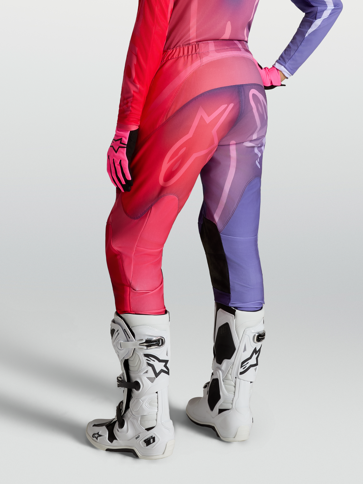 Alpinestars Stella Fluid Kepler Hose, Damen-Motocross-Hose in Lila und Rot, speziell vorgekrümmte Beine mit Stretch-Paneelen, Rückansicht mit Tech-10 Stiefeln und Handschuhen kombiniert.