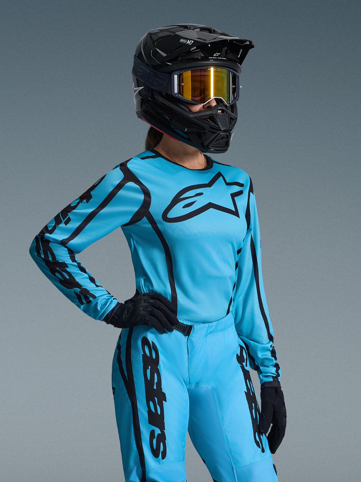 Alpinestars 2026 Damen Stella Fluid Apex Ausrüstungsset, Hellblau und Schwarz, Motocross-Jersey und Hose mit schwarzem Branding, getragen mit schwarzem Helm, gold verspiegelter Brille und schwarzen Handschuhen, spezielle Damenpassform für Offroad-Rennsport