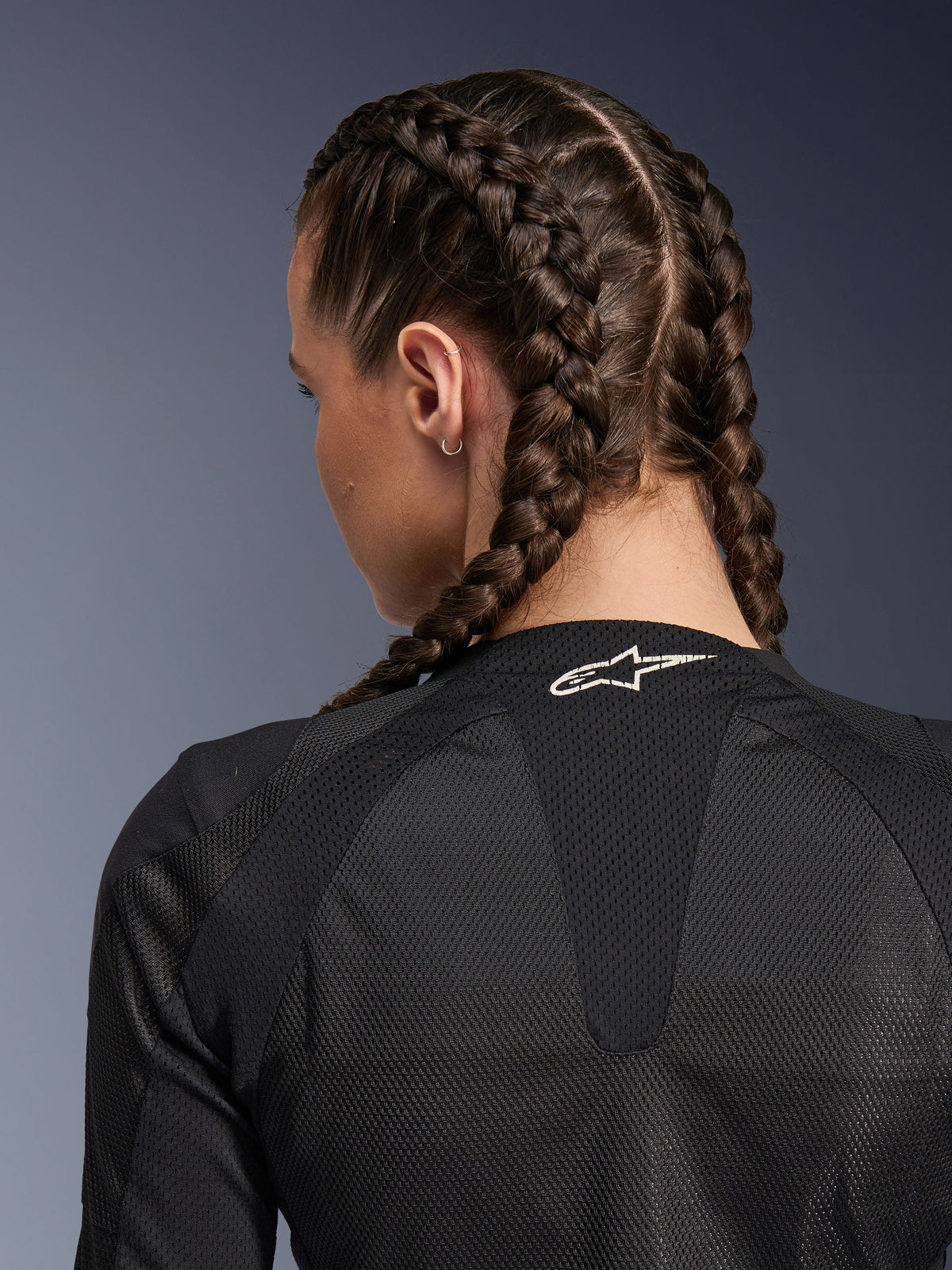 Alpinestars Stella Troop-Air Damenjacke, Schwarz, Detailansicht der Rückseite von oberem Rücken und Nacken, Frau mit französisch geflochtenem Haar, mit weißem Astars-Logo am Kragen und leichtem 2D-Tech-Mesh-Gewebe zur Belüftung