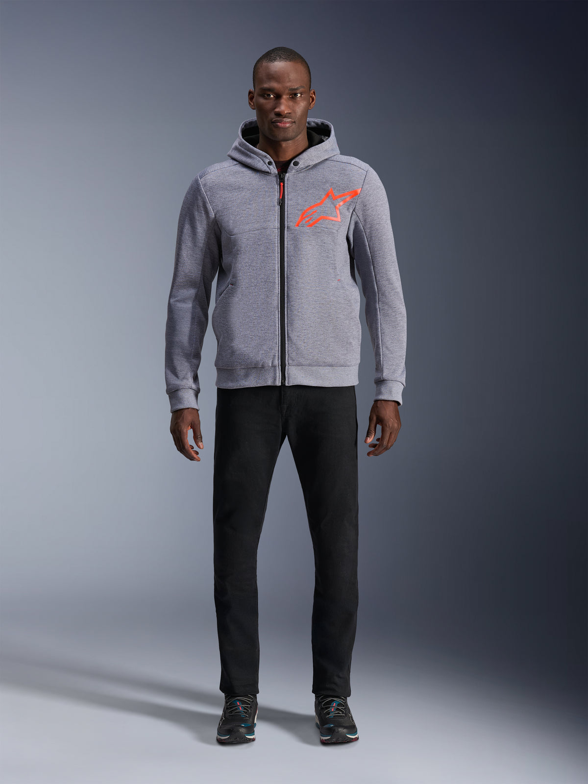 Alpinestars Chrome V2 Sport Kapuzenjacke, urbane Motorradjacke für Herren, Grau-Meliert und Rot Fluo, Tech-Fleece mit Aramid-Verstärkungen, getragen von einem Model mit schwarzer Hose.
