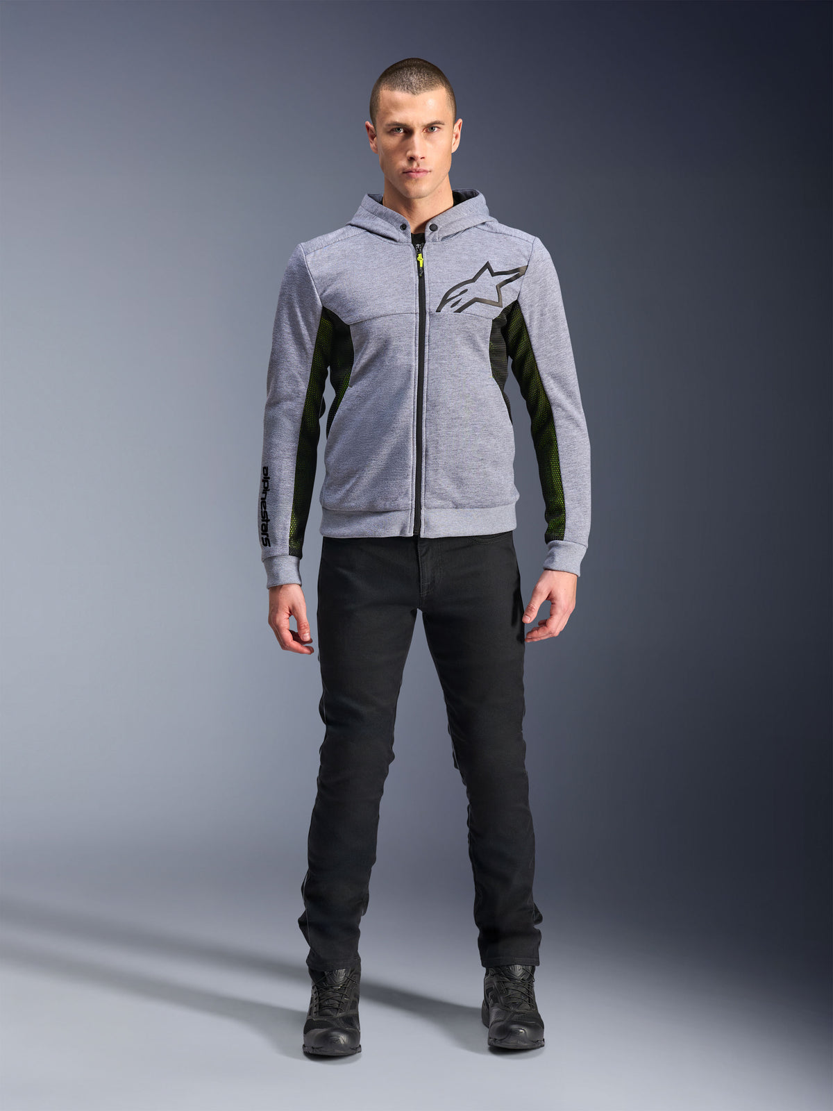 Alpinestars Chrome Air Sport Hoodie, Grau Melange Schwarz, technischer Motorrad-Hoodie mit schwarzen Mesh-Seiteneinsätzen und neongelben Akzenten, schwarzes Stern-Logo auf der Brust, getragen mit schwarzer Hose und Stiefeln, moderner urbaner Fahrstil.