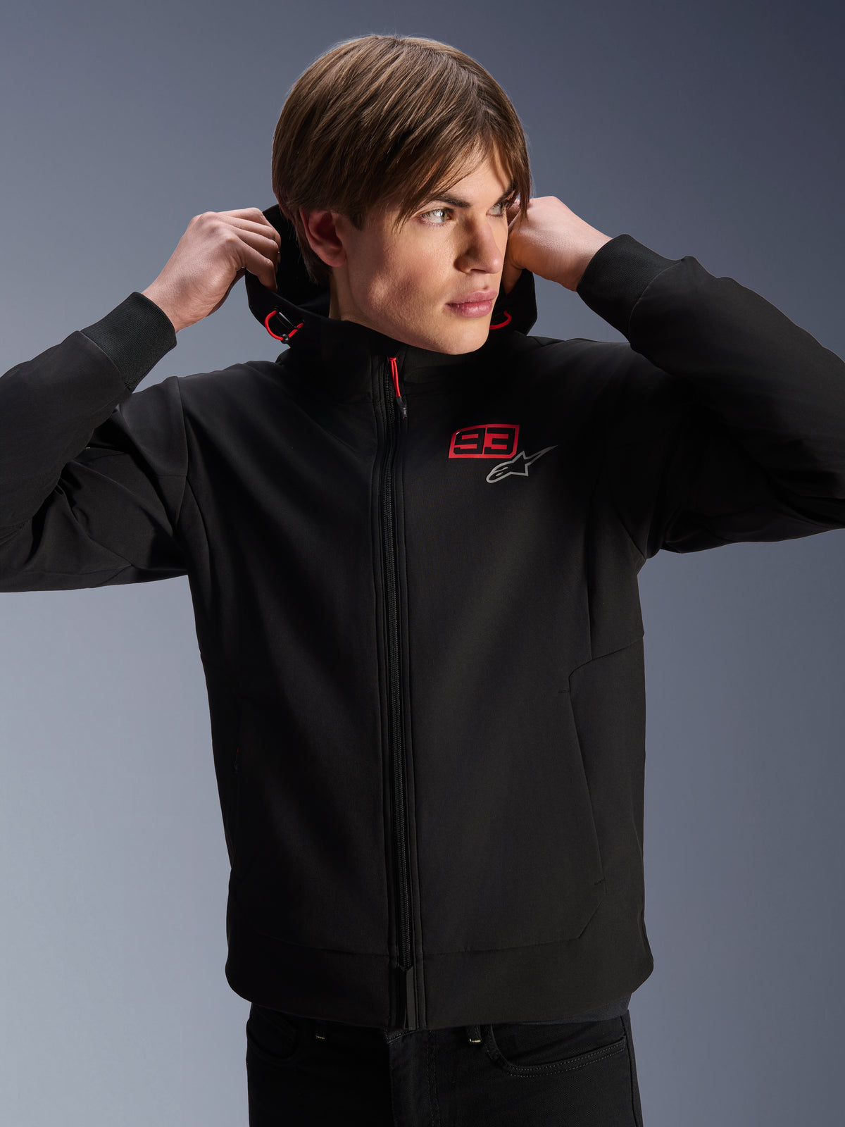 Alpinestars MM93 Radium Tech Hoodie, urbane Motorradjacke, schwarz mit roten und silbernen Logos, getragen von einem männlichen Model, mit durchgehendem Reißverschluss und Rippbündchen, lässige Lifestyle-Motorsportbekleidung