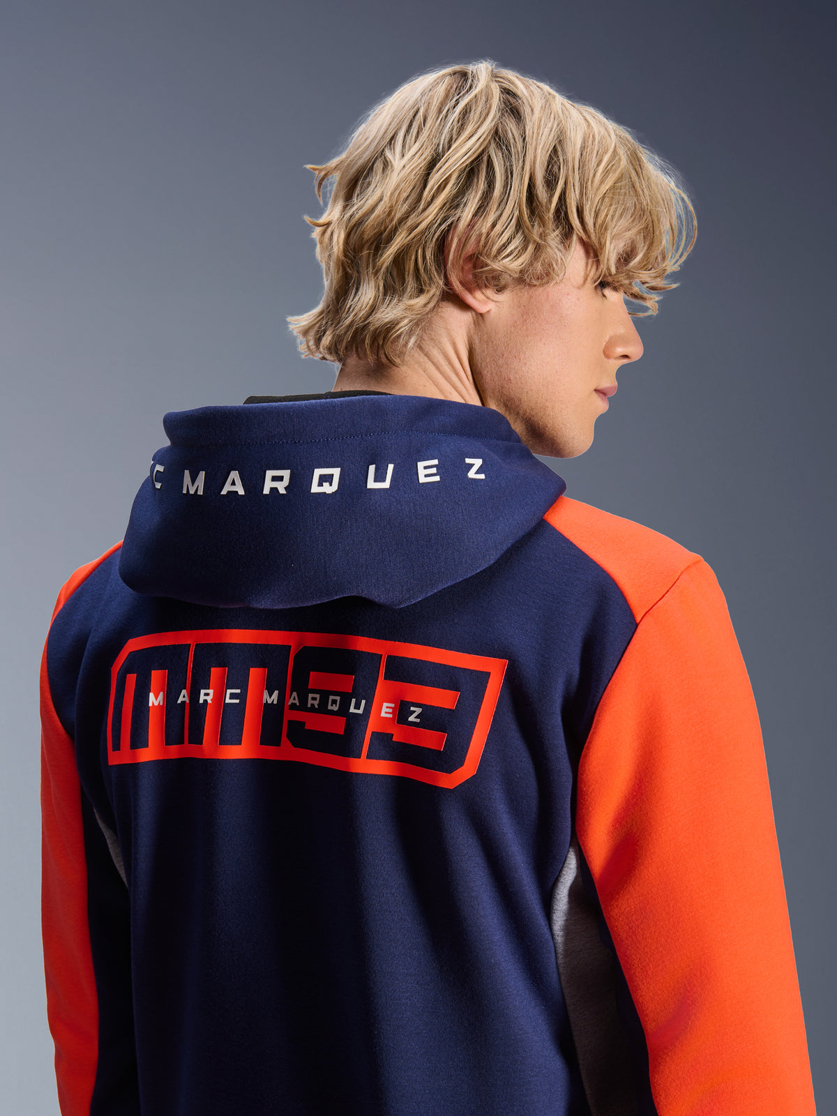 Alpinestars MM93 Chrome V2 Sport Hoodie, marineblau mit leuchtend orangefarbenen Ärmeln, großes rotes MM93-Logo und Marc Marquez-Branding auf dem Rücken, weißer Schriftzug auf der Kapuze, lässiger Urban-Motorrad-Hoodie.