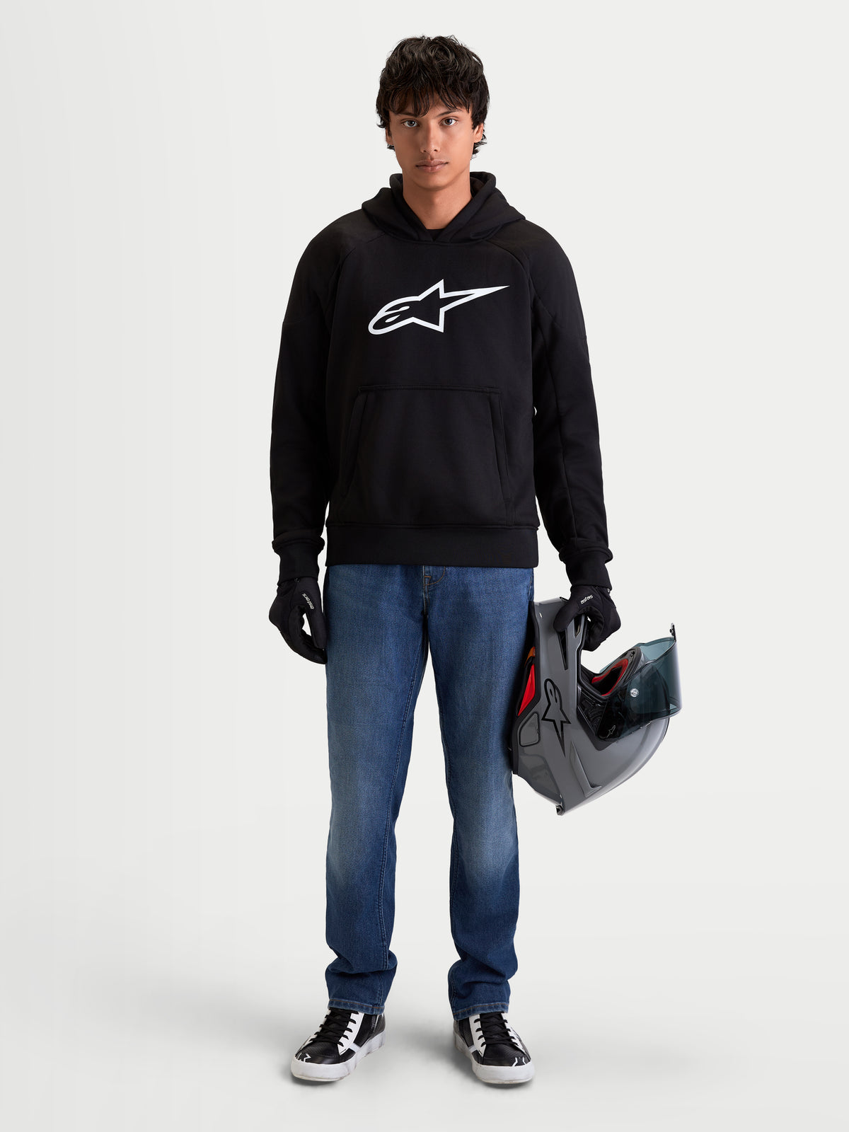 Alpinestars Ageless Kapuzenpullover, schwarzer urbaner Motorrad-Kapuzenpullover mit weißem Astar-Logo auf der Brust, getragen von einem Model mit Helm und Motorradhandschuhen, lässige CE-zertifizierte Schutzausrüstung