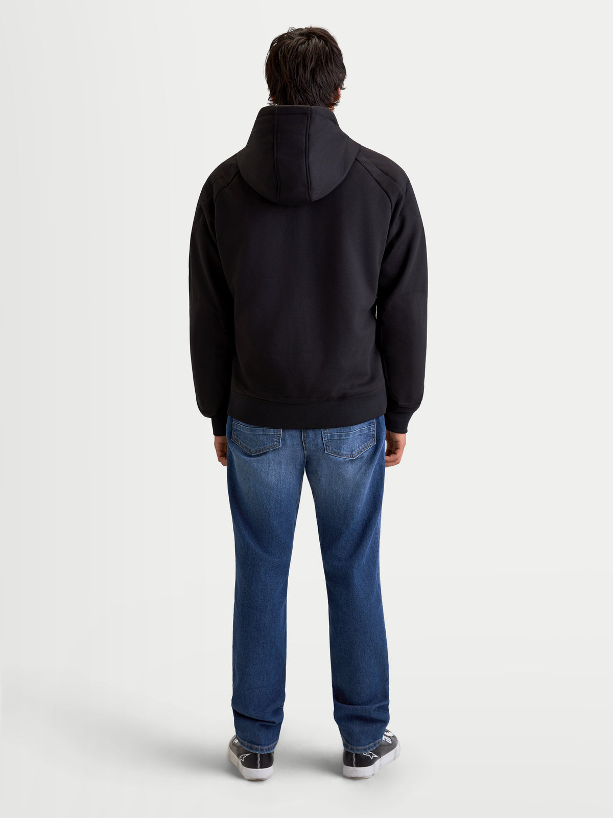 Alpinestars Ageless Hoodie, urbaner Motorrad-Kapuzenpullover für Herren in Schwarz, Rückansicht am Model mit Jeans und Freizeit-Motorradschuhen, mit fester Kapuze und schützender Textilkonstruktion