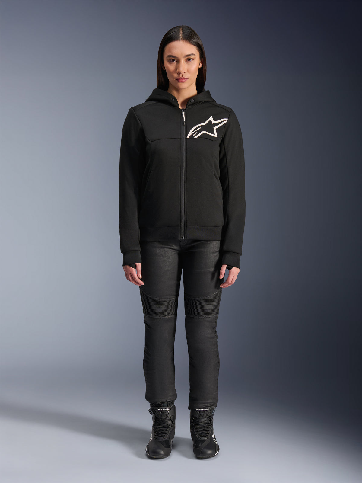 Alpinestars Stella Chrome V2 Sport Hoodie für Damen, Schwarz mit weißem Astars-Logo auf der Brust, kombiniert mit schwarzer technischer Motorradhose und Stiefeln, urbanes Motorradbekleidungs-Design