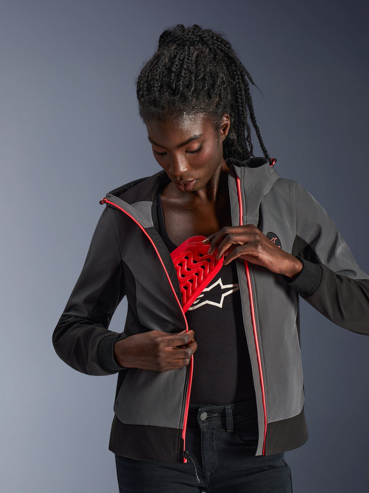 Alpinestars Woman Stella Radium Tech Hoodie in Deep Gray and Black, model demonstrating the removable red Nucleon Flex Plus armor, urban motorcycle hoodie with pink zipper accents.