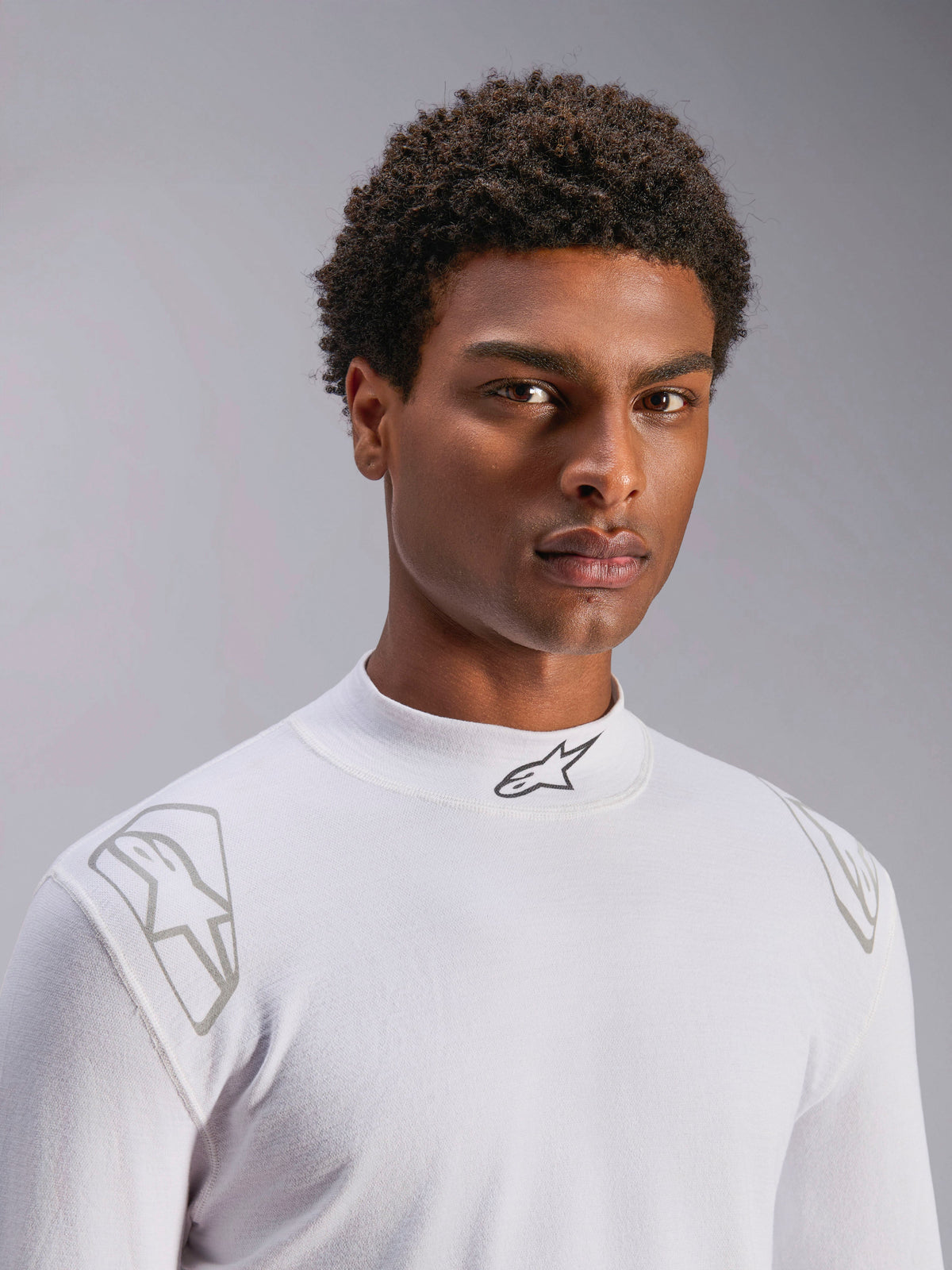 Alpinestars ZX Evo V3 Langarm-Oberteil, weißer Auto-Rennsport Base Layer, von einem männlichen Model getragen, Stehkragen mit schwarzem Alpinestars-Logo, silberne Grafikdrucke auf den Schultern, leichte flammhemmende Motorsport-Unterwäsche