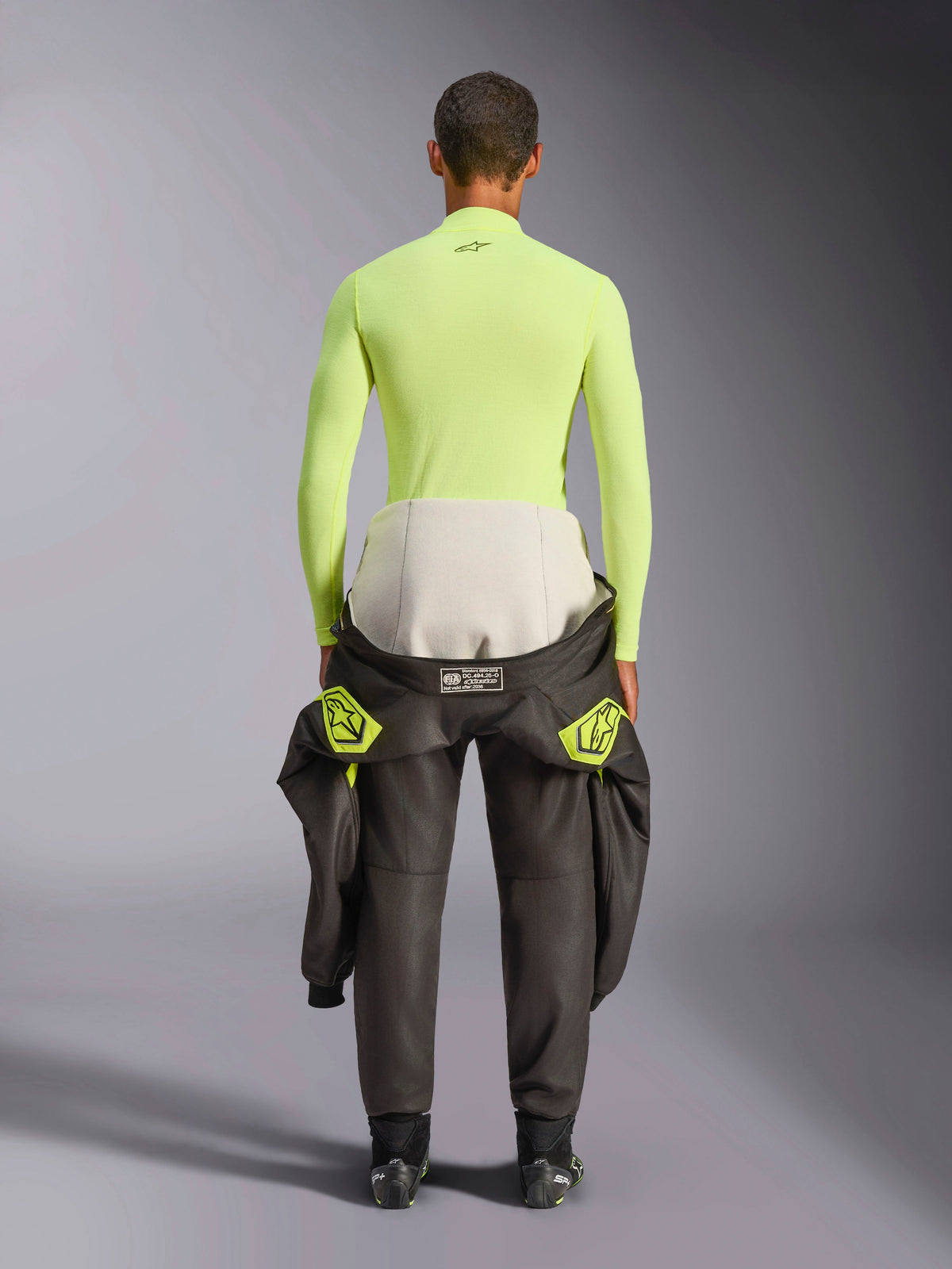 Alpinestars ZX Evo V3 Top, Long Sleeve Base Layer, Yellow Fluo, back view of a driver with a racing suit tied around the waist, vibrant neon yellow flame-resistant top featuring a small black logo on the neck and a slim athletic fit