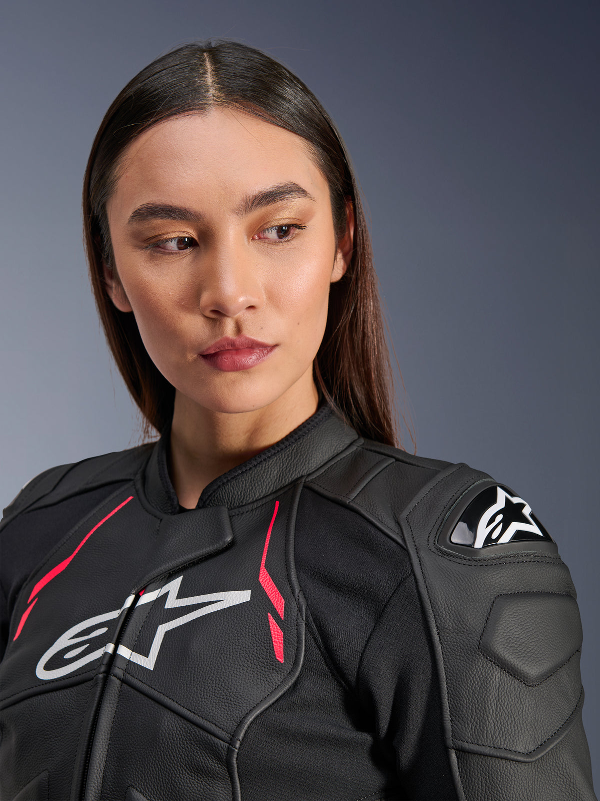 Frau in der Alpinestars Stella Dusk Lederjacke in Schwarz Diva Pink Weiß, mit weißem Brustlogo, leuchtend pinkfarbenen Akzenten und externem DFS-Schulterschutz, erstklassige Motorradausrüstung aus Rindsleder