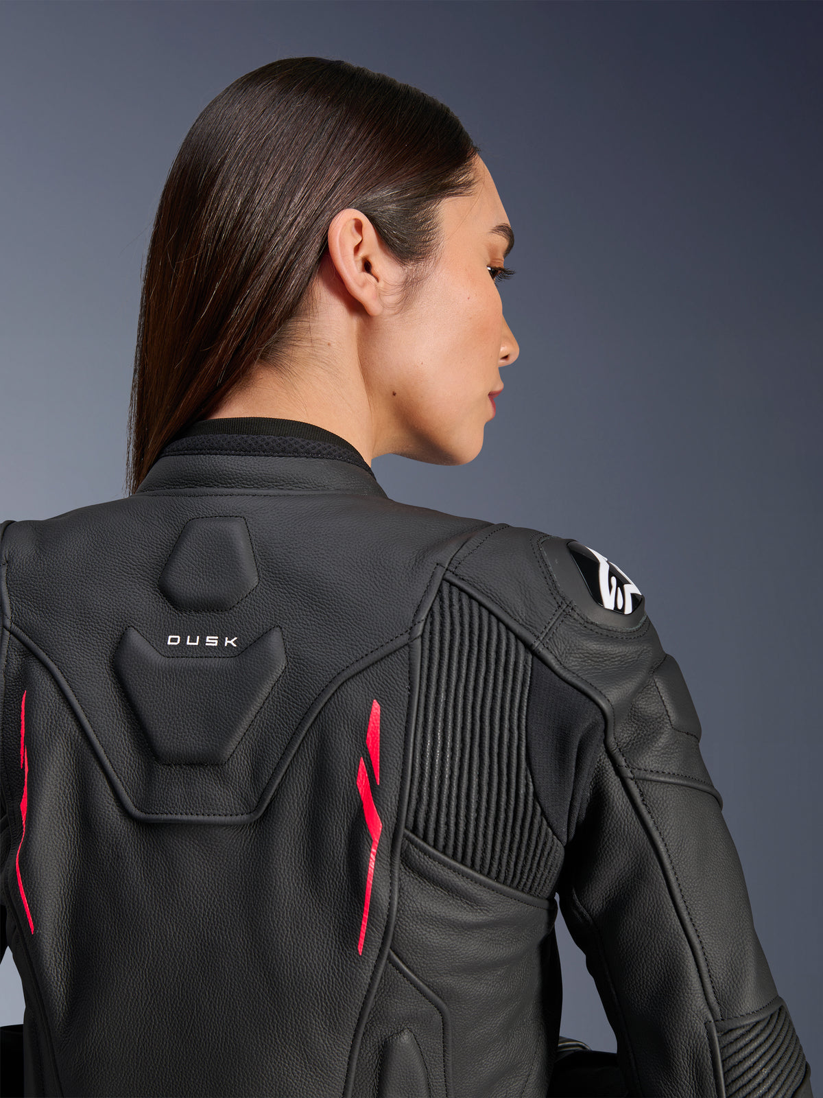 Frau trägt Alpinestars Stella Dusk Lederjacke, schwarzes Leder mit Diva Pink Akzenten und weißem Logo auf der Schulter, Rückansicht mit DUSK-Branding und Akkordeon-Stretcheinsätzen, sportliches ergonomisches Design