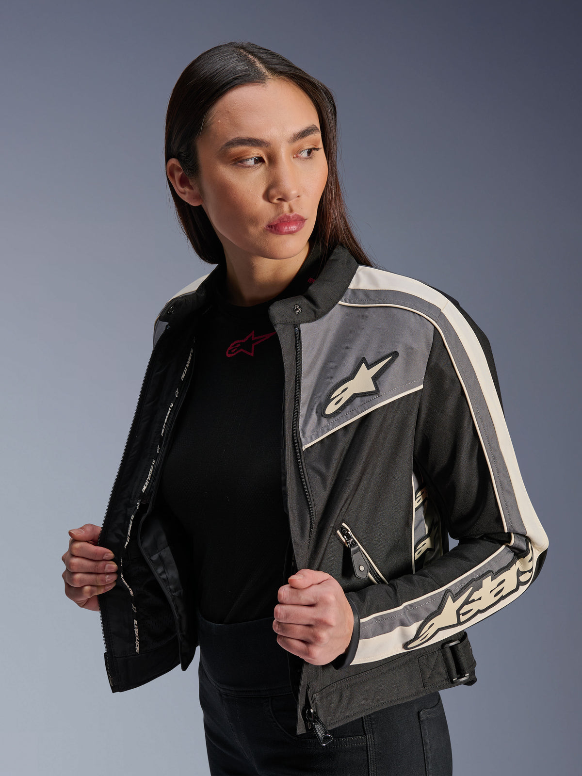 Alpinestars Stella T-Dyno WR Damenjacke, Textil-Motorradjacke, Schwarz, Dunkelgrau und Ecru, vintage-inspiriertes Design mit sportlichen Streifen und Logos auf Brust und Ärmeln, getragen von einem Model, urbane Motorradbekleidung
