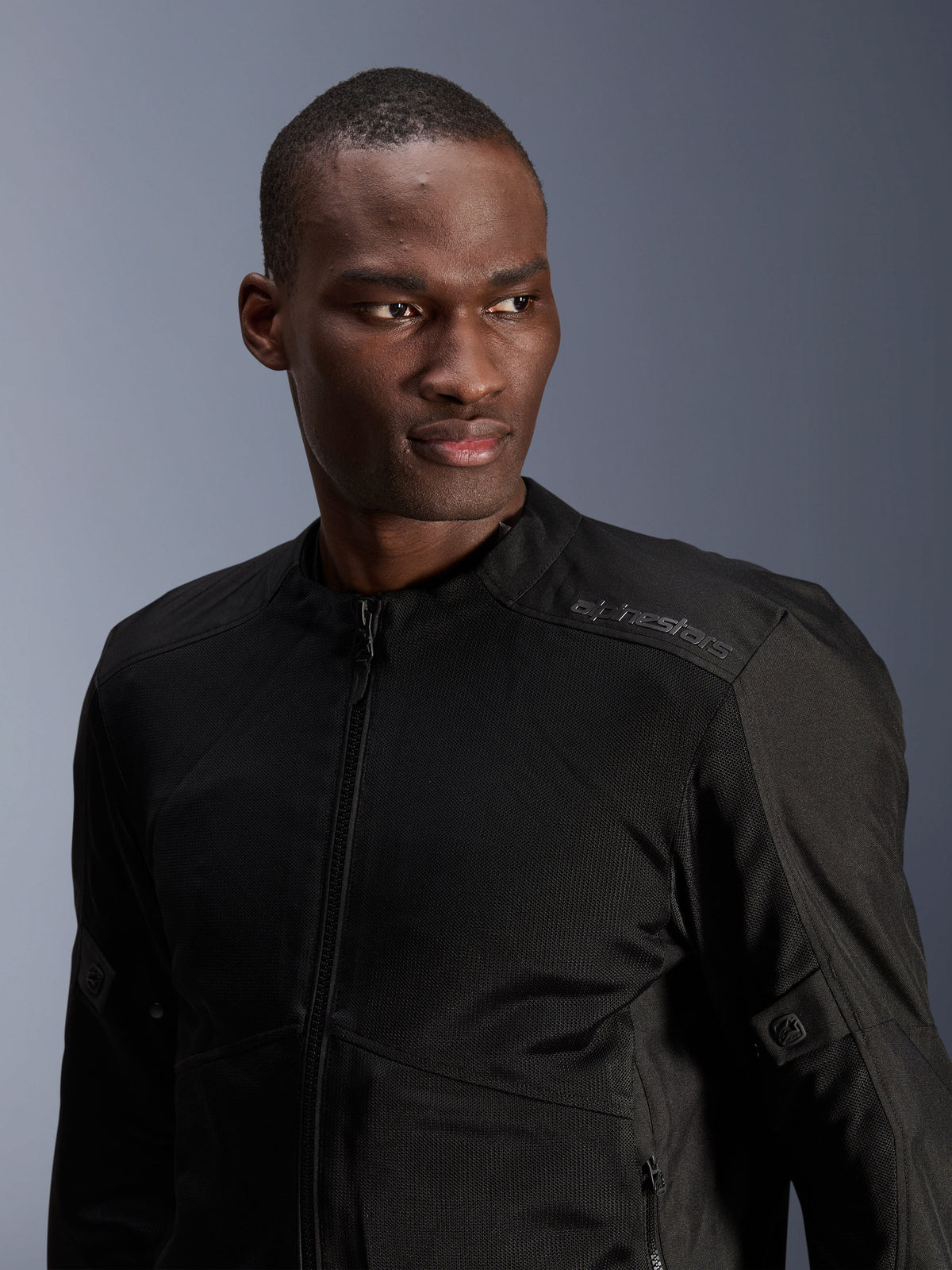 Alpinestars C-1 Air Jacke, Schwarz, urbane Motorradjacke mit Tech-Mesh-Einsätzen, von einem Model getragen, mit dezentem Alpinestars-Wärmeübertragungslogo auf der Schulter, entwickelt für Luftzirkulation und leichten Tragekomfort bei warmem Wetter