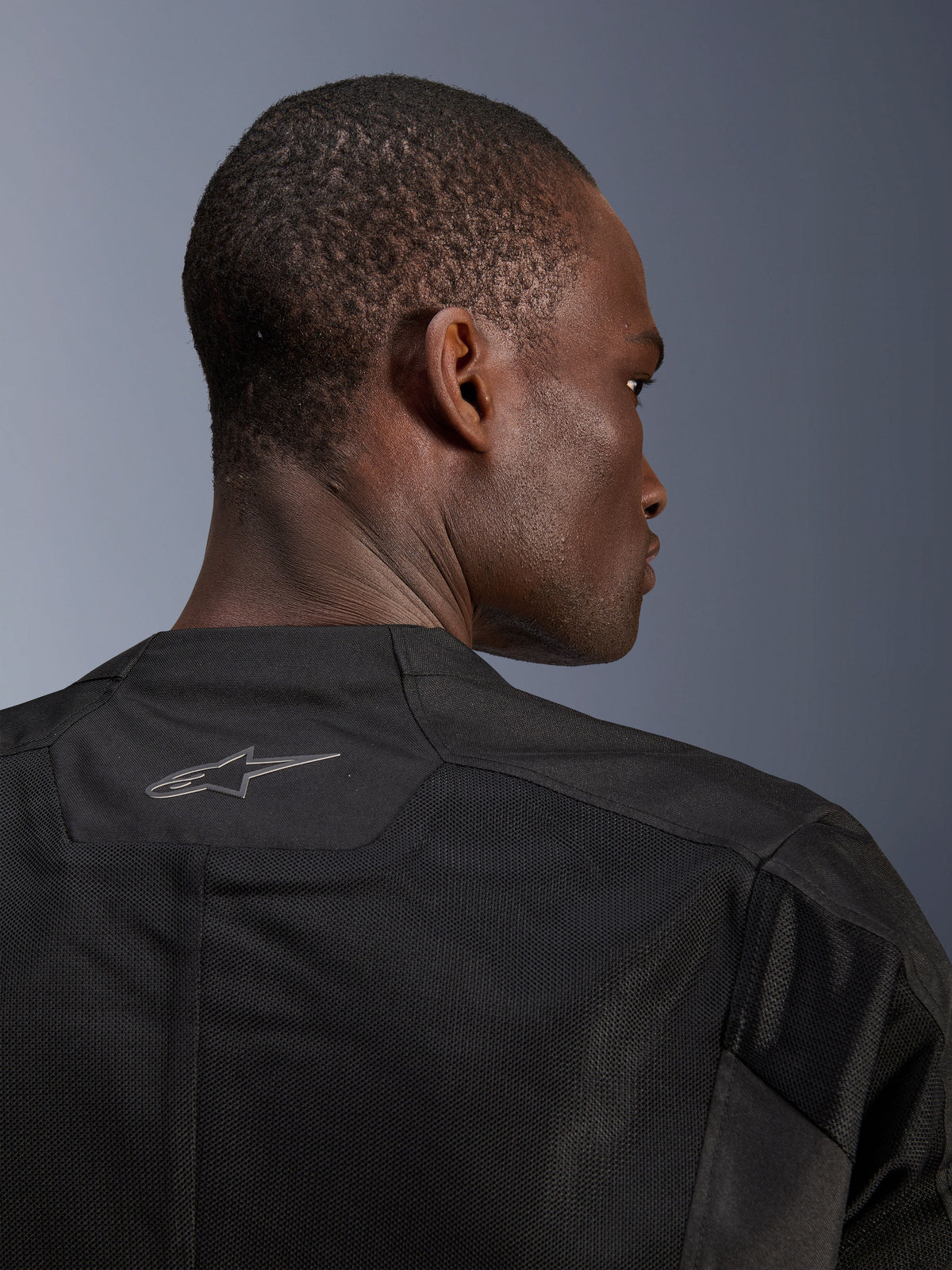 Alpinestars C-1 Air Jacke, schwarze Motorradjacke, Nahaufnahme der Rückseite mit atmungsaktiven Tech-Mesh-Einsätzen und einem reflektierenden Alpinestars-Logo am Kragen, urbane Motorradausrüstung