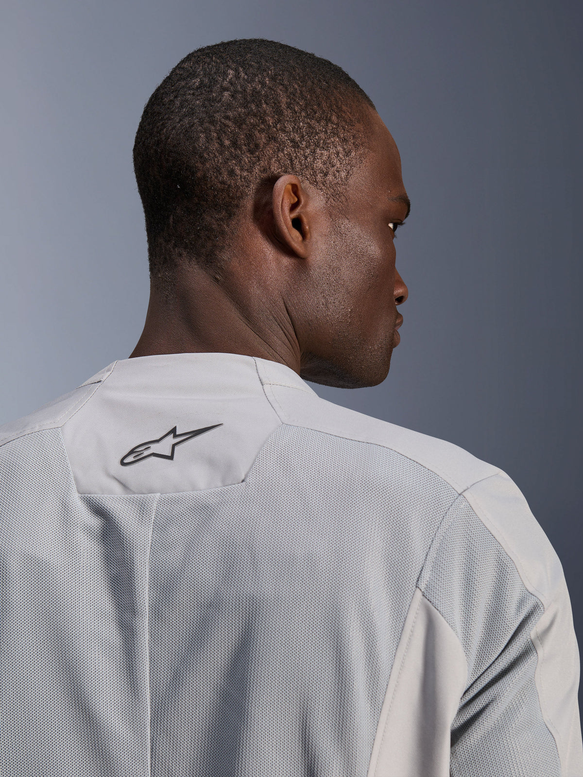 Alpinestars C-1 Air Jacke, silbergraue Textil-Motorradjacke, Nahaufnahme der Rückseite mit Tech-Mesh-Einsätzen für Luftzirkulation und schwarzem Alpinestars-Logo auf dem oberen Rücken, urbane Fahrer-Ästhetik