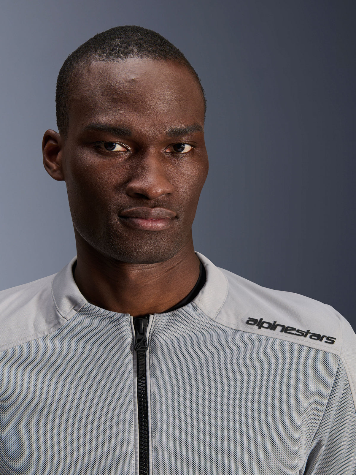 Alpinestars C-1 Air Jacke in Silber und Grau, Nahaufnahme-Porträt eines männlichen Fahrers, mit technischen Mesh-Einsätzen und schwarzem Branding auf der Schulter, urbane zeitgemäße Motorradausrüstung
