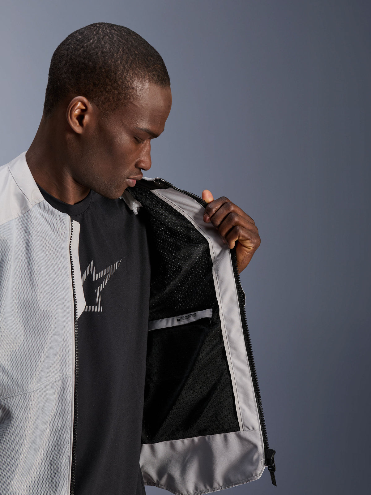 Männliches Model trägt die Alpinestars C-1 Air Jacke in Silber und öffnet die Vorderseite, um das schwarze Tech-Mesh-Innenfutter und eine wasserdichte Innentasche mit Reißverschluss zu zeigen.