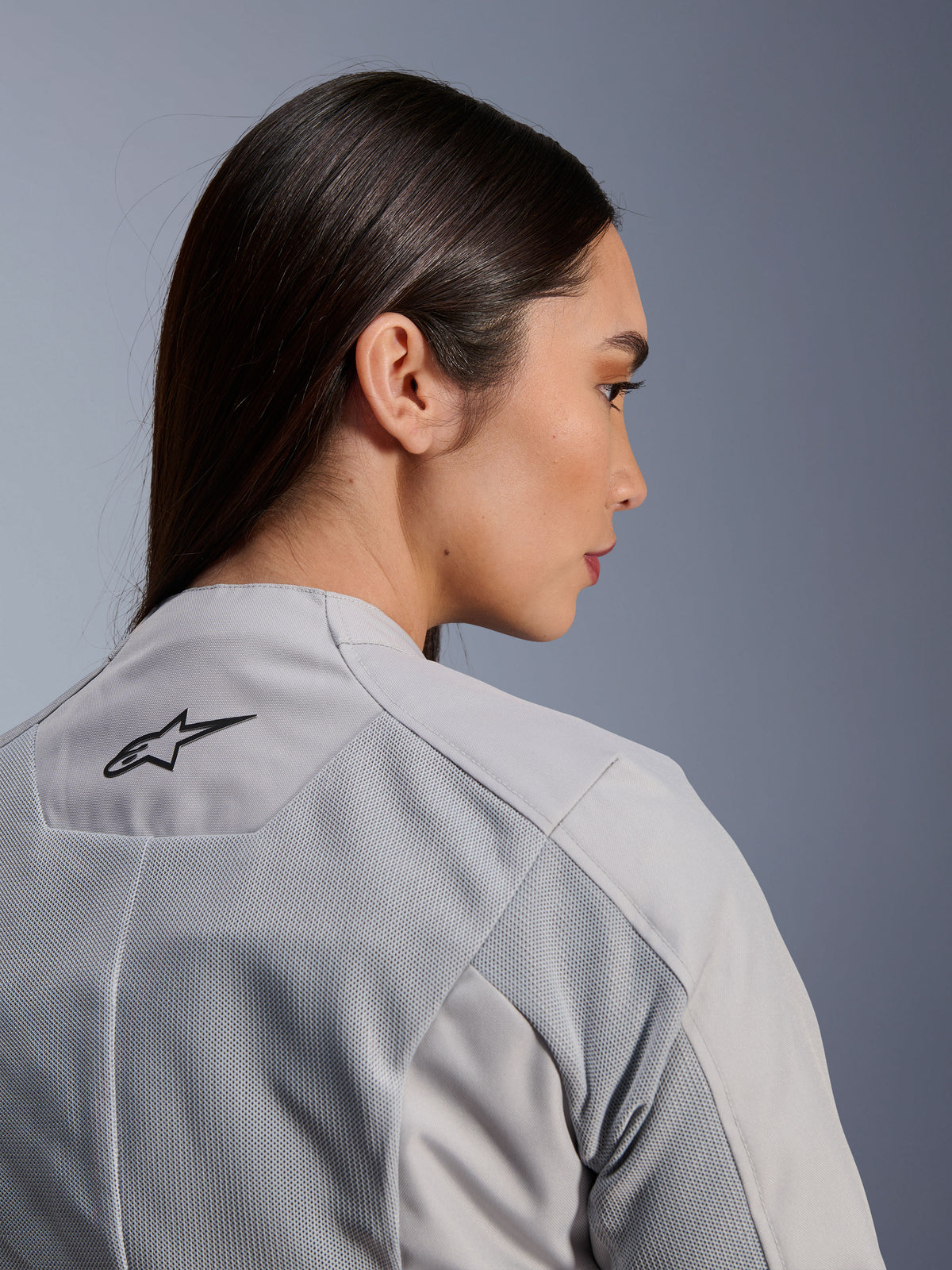 Frau in der Alpinestars Stella C-1 Air Jacke in Silber, Nahaufnahme der Seiten-Rückansicht, schwarzes Alpinestars-Logo, Tech-Mesh-Belüftungseinsätze, klares, zeitgemäßes urbanes Motorrad-Design