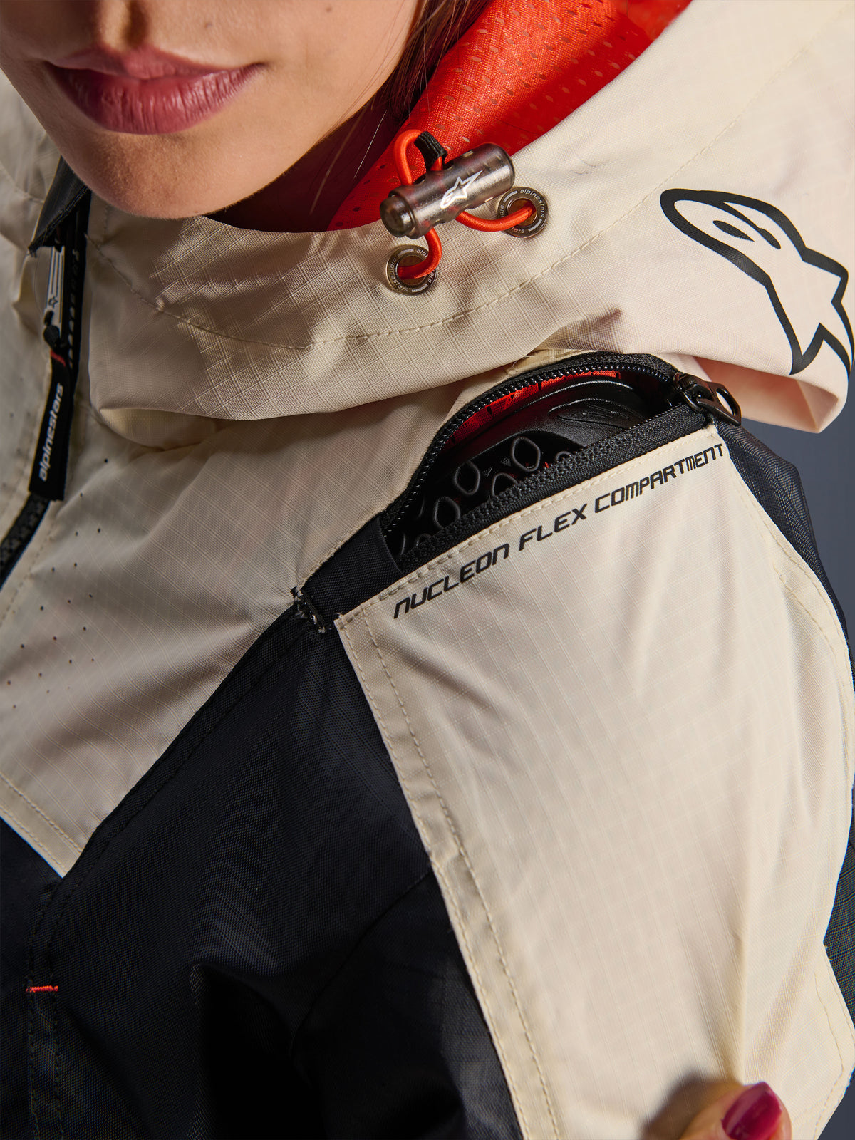 Alpinestars Molly Air Jacket, Women's Motorcycle Jacket, Black Almond, close-up view of the shoulder showing the Nucleon Flex Compartment zipper, ripstop fabric, and orange mesh lining inside the hood