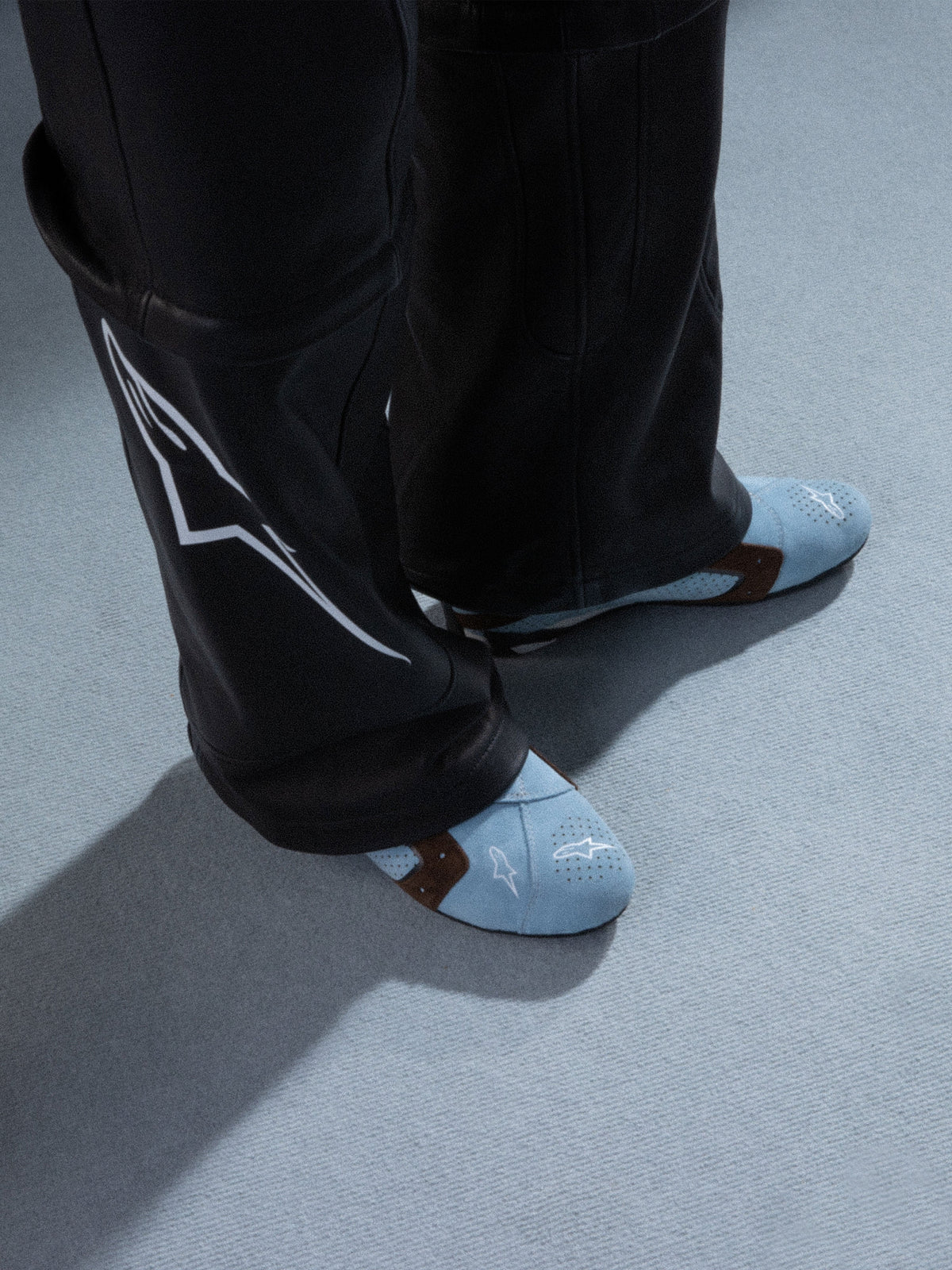 Alpinestars RSRV Starline Schuhe, Hellblaue Lifestyle-Sneaker mit perforierten Mustern, Braune Akzente, Weiße Logo-Details, Premium-Leder, Getragen mit schwarzer Lederhose