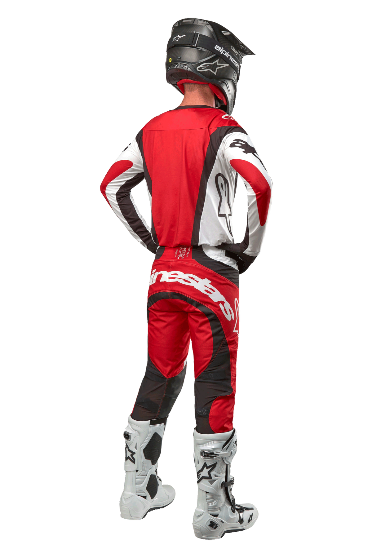 Alpinestars 2024 Techstar Ocuri Hose, Motocross-Hose, Mars Rot Weiß Schwarz, Rückansicht eines Motocross-Fahrers in kompletter Rennausrüstung, einschließlich passendem Jersey, schwarzem Helm und weiß-schwarzen Stiefeln, hebt das Alpinestars-Branding und die strapazierfähige Stoffkonstruktion hervor.