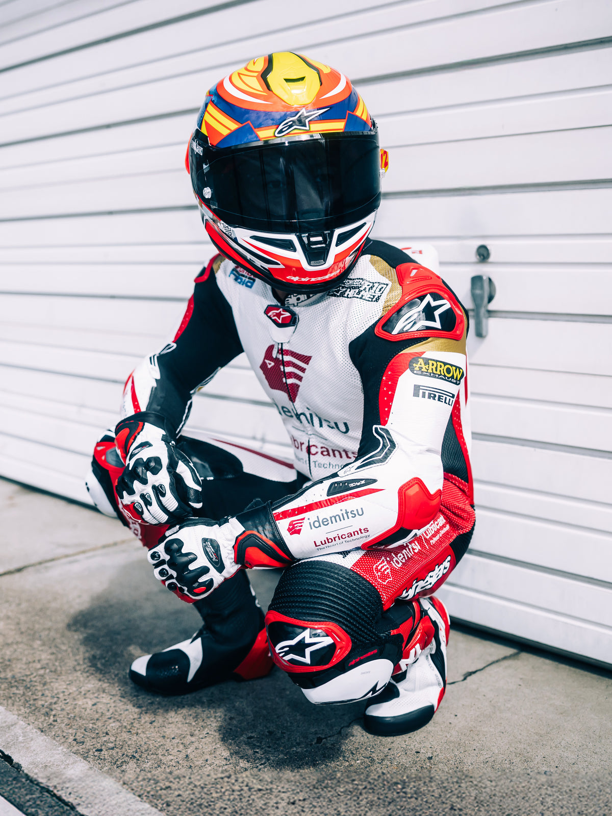 Alpinestars S-R7 Taiyo Furusato Helm, Integral-Motorradrennhelm, Rot, Weiß, Blau und Neongelb, ECE 22.06-zertifiziert, getragen von einem Motorradrennfahrer in voller Lederkombi mit getöntem Visier.