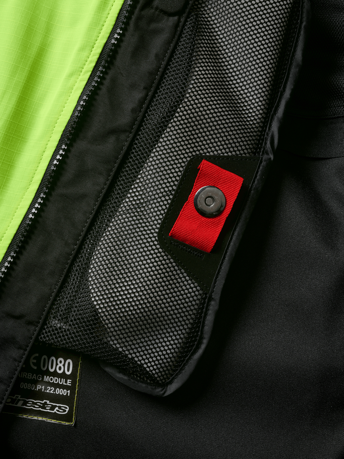 Alpinestars Tech-Air® 3 V2 System Detailansicht, Nahaufnahme der internen Netztasche mit roter Zuglasche und Druckknopf, leuchtend gelbes fluoreszierendes Panel, schwarze Textilkonstruktion mit Airbag-Modul-Etikett und Reißverschluss
