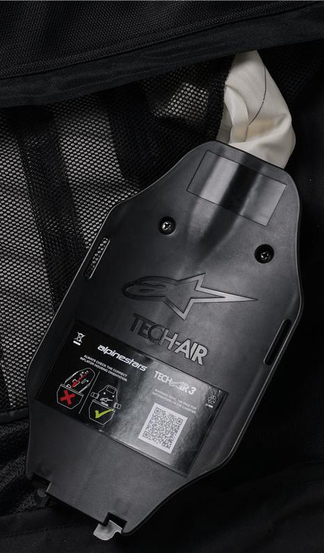 Alpinestars Tech-Air 3 V2 System, Innenansicht des Gasaufbläsers und des ECU-Gehäuses, schwarzer Kunststoff mit geprägtem Logo, Sicherheitsetikett mit QR-Code und Installationsdiagrammen, schwarzes Mesh-Innenfutter, Detail des benutzerwartbaren autonomen Airbag-Systems