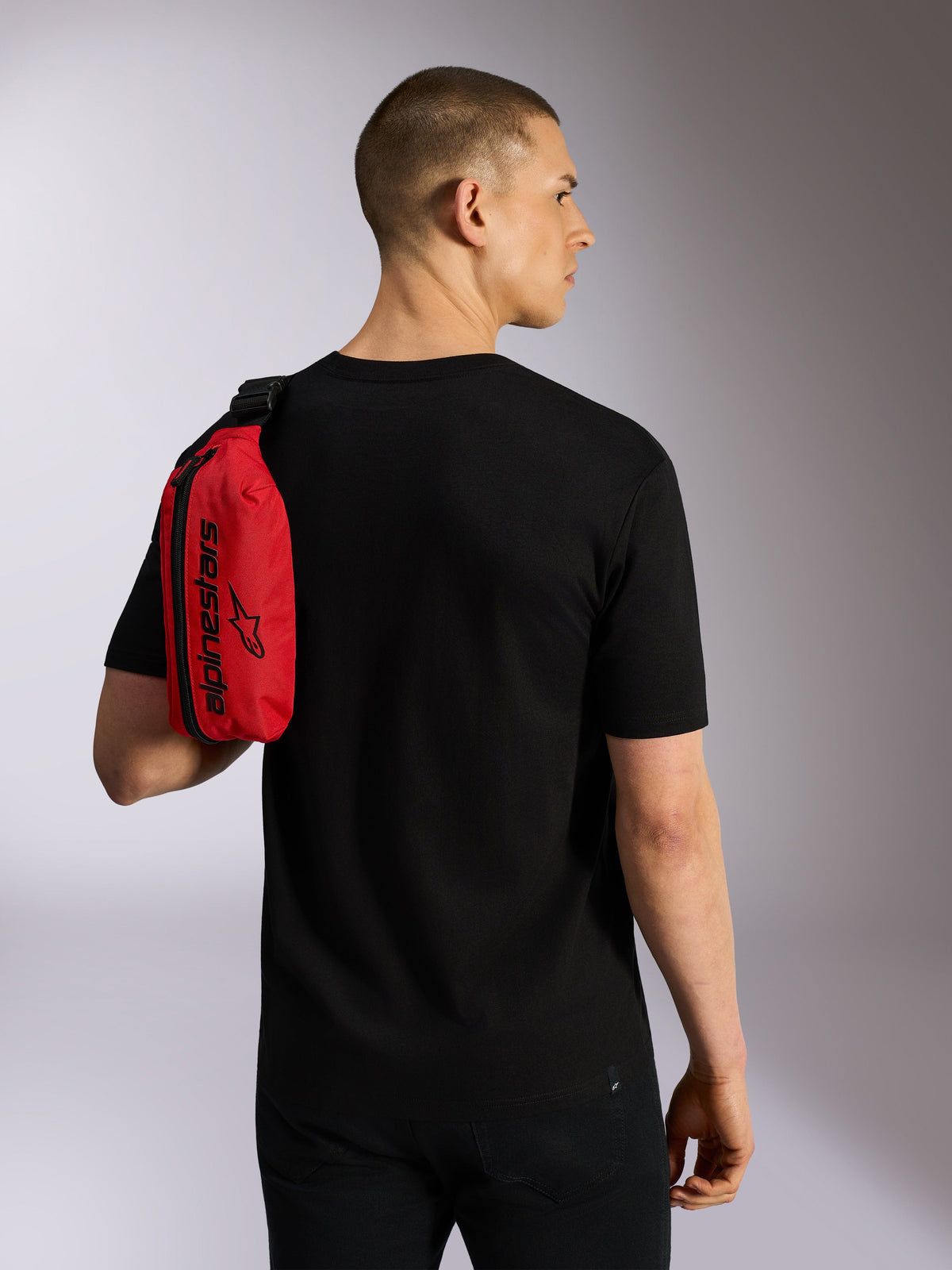 Alpinestars Only Linear Hüfttasche, Rot und Schwarz, von einem Modell in einem schwarzen T-Shirt als Sling-Tasche über die Schulter getragen, mit vertikalem Reißverschluss und schwarzem Alpinestars-Branding, langlebiges urbanes Accessoire.