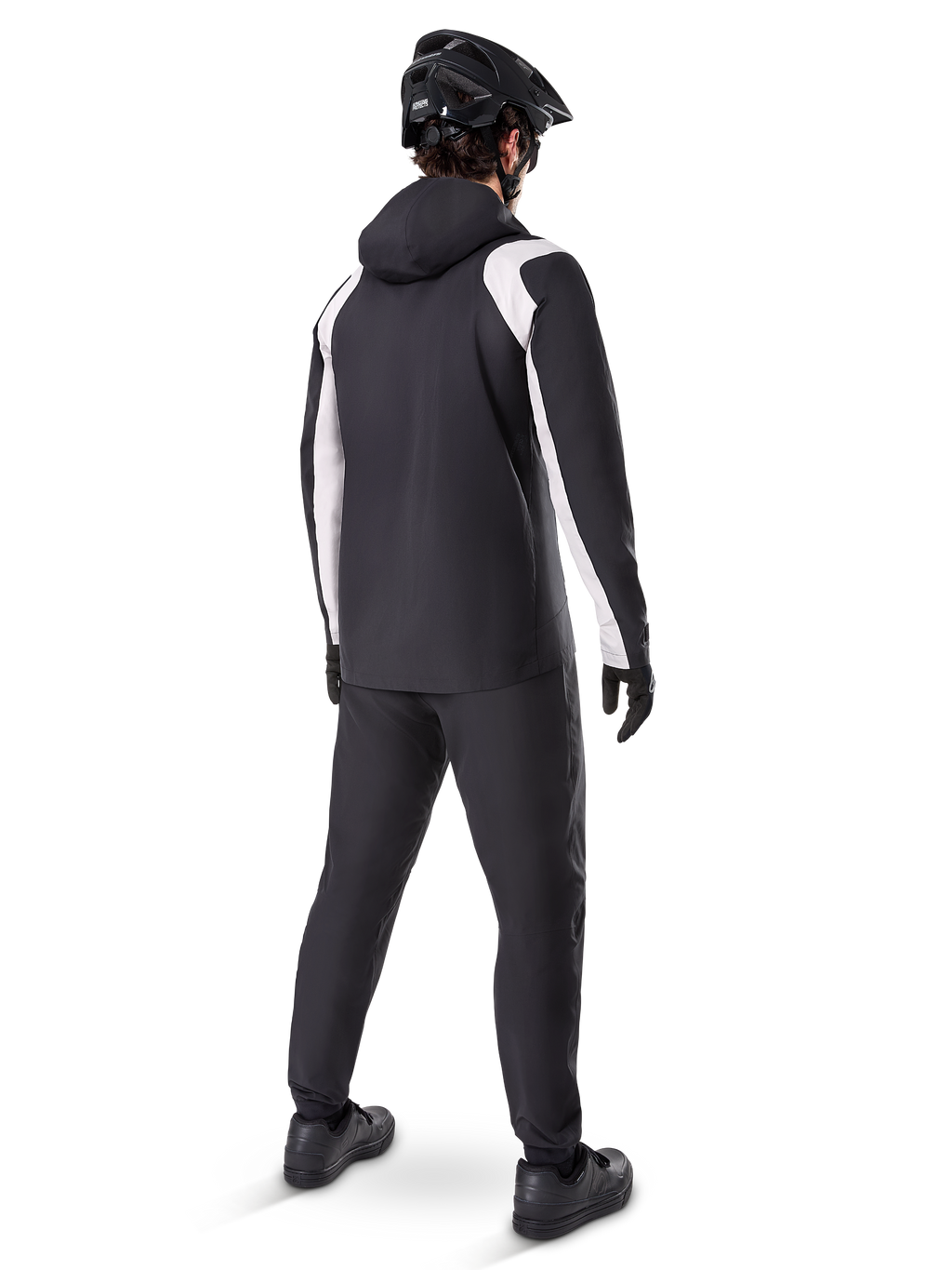 Alpinestars A-Dura Regenjacke, Rückansicht eines männlichen Radfahrers in der schwarz-weißen wasserdichten MTB-Jacke, dazu passende schwarze Radhose, schwarzer Helm und Handschuhe, technische Ausrüstung für das Mountainbiken bei nassen Bedingungen.