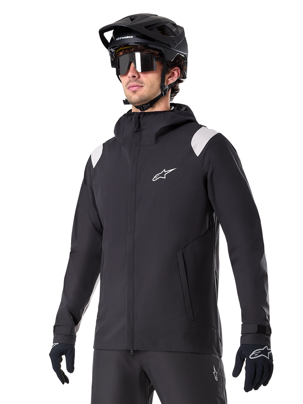 Alpinestars A-Dura Regenjacke, Mountainbike-Regenjacke, Schwarz mit hellgrauen Schulterakzenten, getragen von einem Fahrer mit schwarzem MTB-Helm und Sonnenbrille, weißes Logo auf der Brust, wasserdichte Konstruktion, kombiniert mit schwarzer Hose und Handschuhen für den Offroad-Radsport