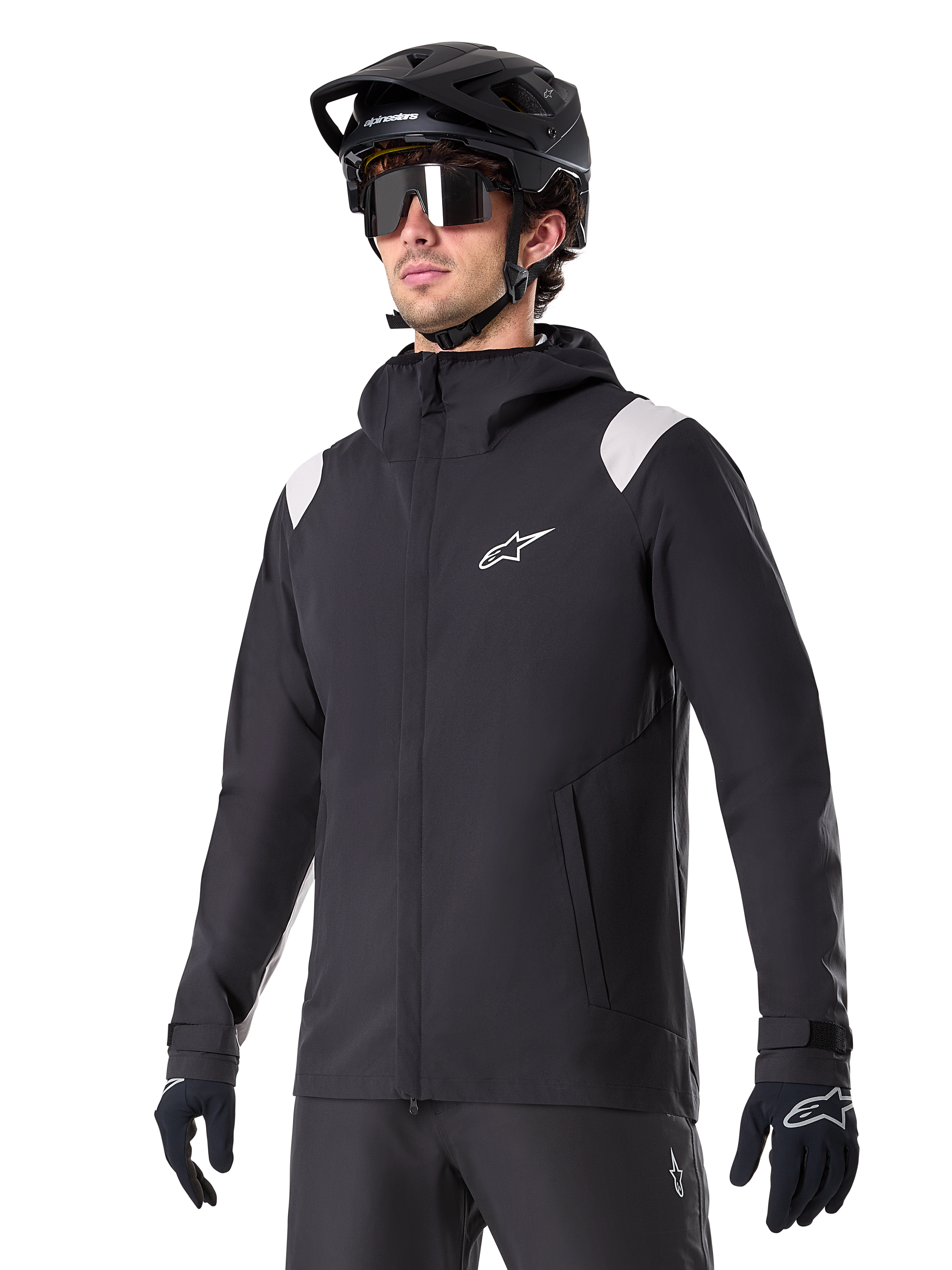 Alpinestars A-Dura Regenjacke, Mountainbike-Regenjacke, Schwarz mit hellgrauen Schulterakzenten, getragen von einem Fahrer mit schwarzem MTB-Helm und Sonnenbrille, weißes Logo auf der Brust, wasserdichte Konstruktion, kombiniert mit schwarzer Hose und Handschuhen für den Offroad-Radsport