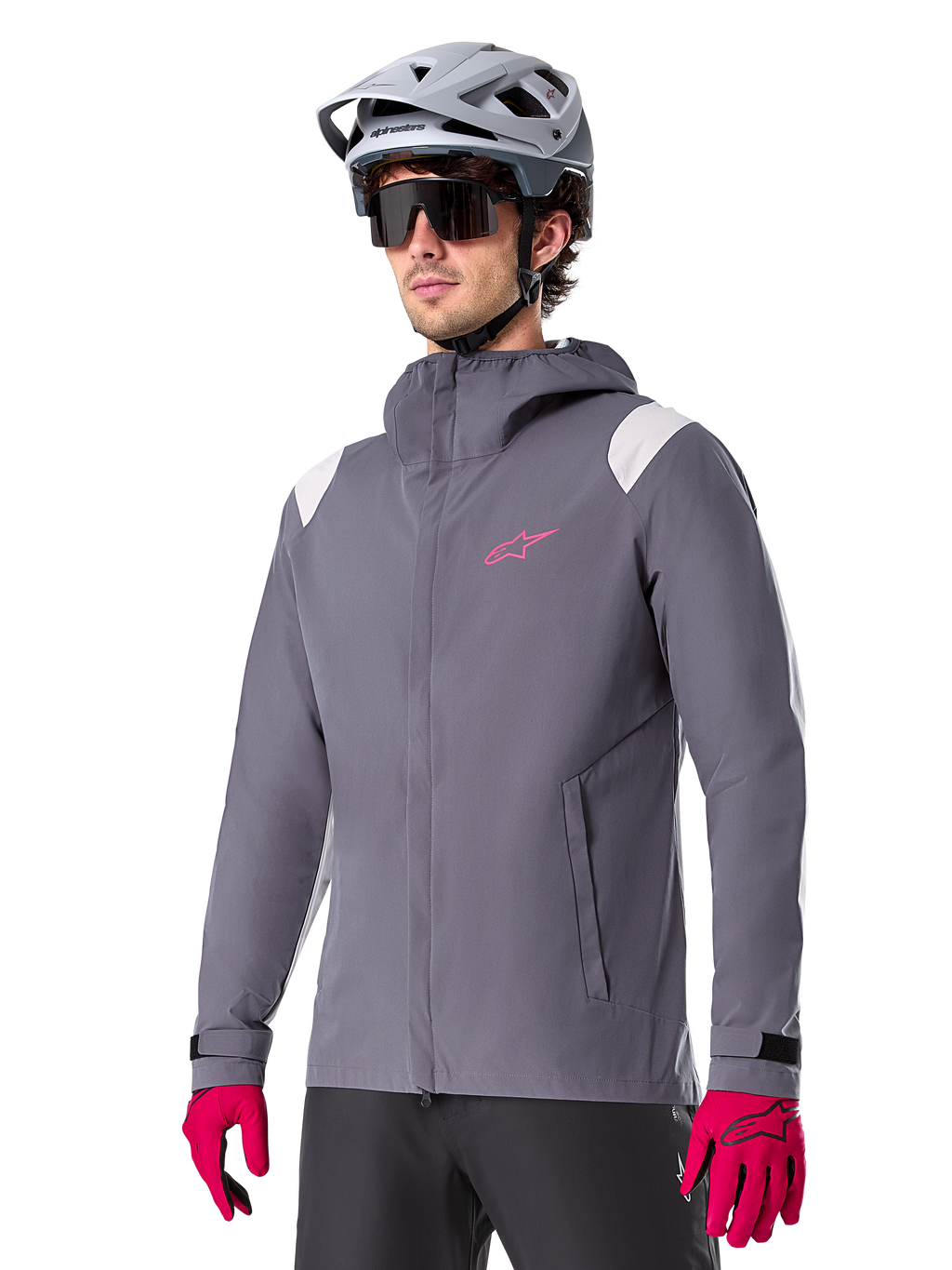 Alpinestars A-Dura Regenjacke, Mountainbike-Regenjacke, Dark Titanium Grau mit pinkem Logo und weißen Schulterakzenten, Kapuzendesign mit Fronttaschen, getragen mit pinken Handschuhen und einem hellgrauen Fahrradhelm