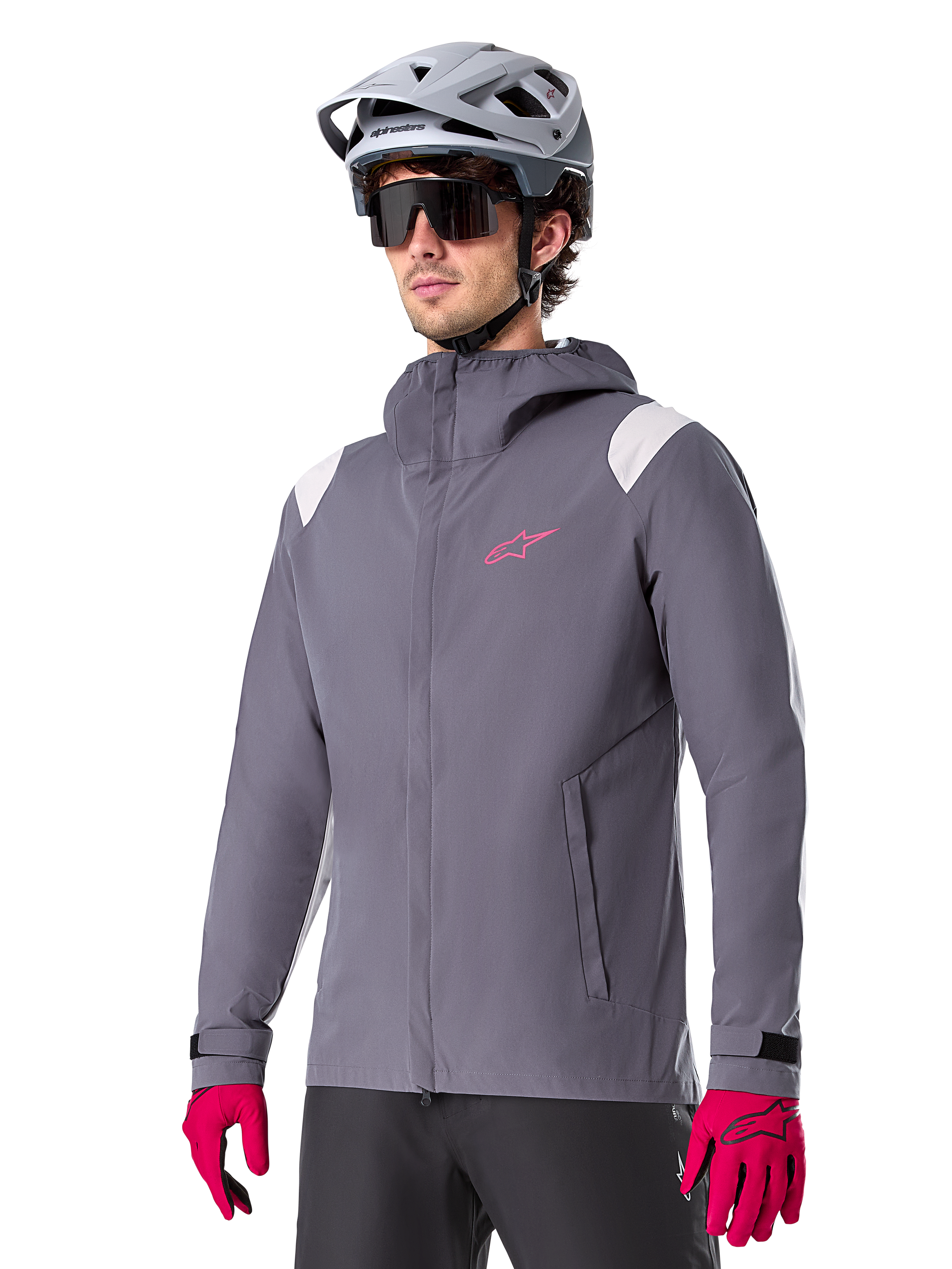 Alpinestars A-Dura Regenjacke, Mountainbike-Regenjacke, Dark Titanium Grau mit pinkem Logo und weißen Schulterakzenten, Kapuzendesign mit Fronttaschen, getragen mit pinken Handschuhen und einem hellgrauen Fahrradhelm