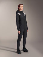 Frau in der Alpinestars Stella A-Dura Regenjacke in Schwarz, 2,5-lagiges wasserdichtes MTB-Shell mit hellgrauen Schulterakzenten, passender schwarzer Hose und Fahrradschuhen, Studioporträt für Performance-Radsportbekleidung