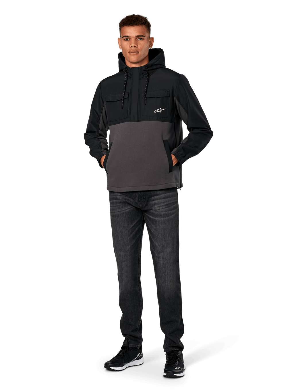Alpinestars Juncture Hybrid Jacket, Black and Gunmetal, mixed-material anorak hoodie featuring a canvas fleece body and ripstop overlays, white A-star logo on chest, drawstring hood, worn by model with dark jeans and black sneakers, casual motorsport-inspired streetwear