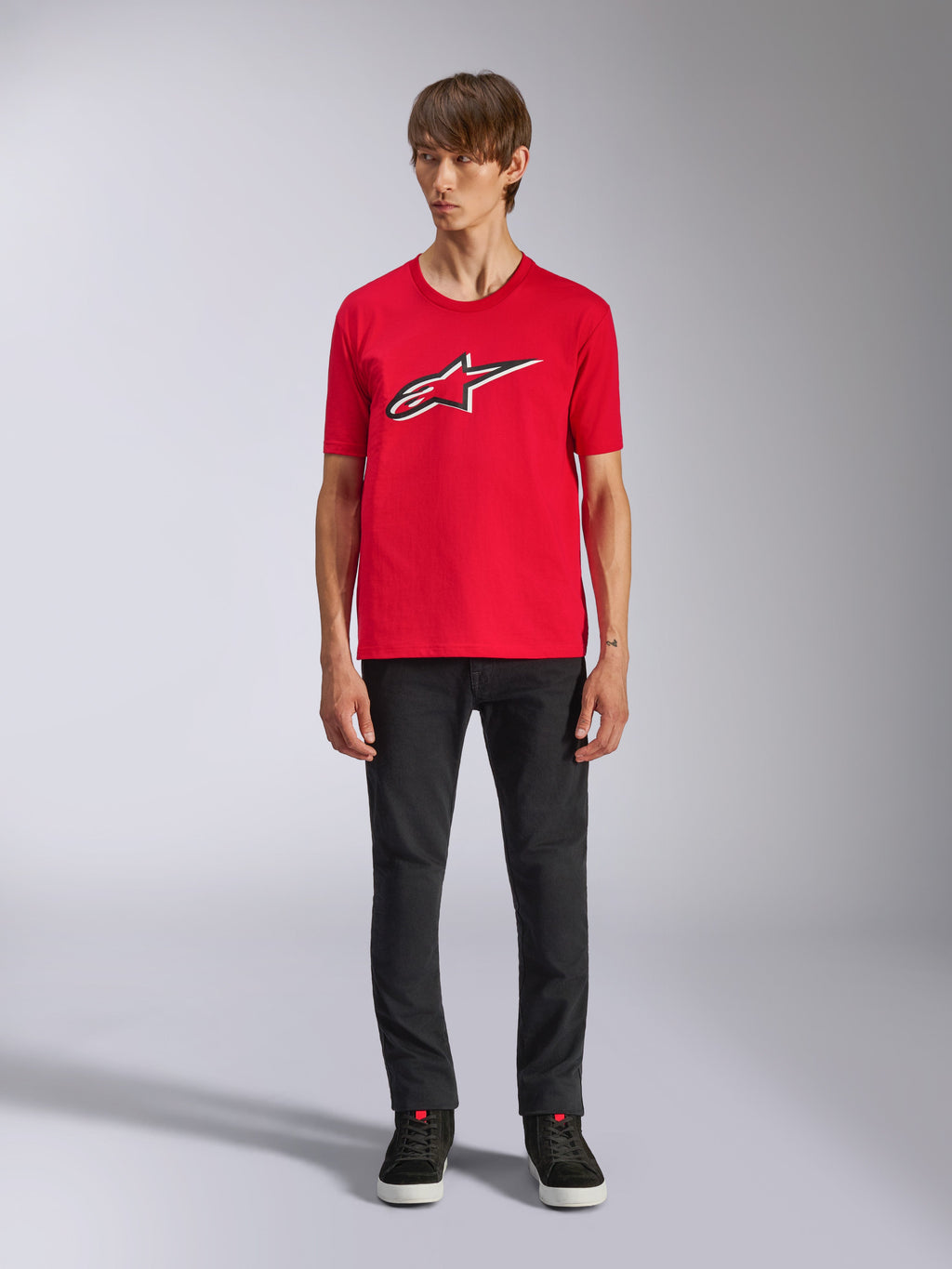 Alpinestars Ageless Shadow CSF Tee, Kurzarm-T-Shirt, Rot, vorderseitiges Ageless-Logo mit weißen und schwarzen Umrissen, getragen von einem Modell mit schwarzer Hose und Sneakern, lässige Motorsport-Streetwear